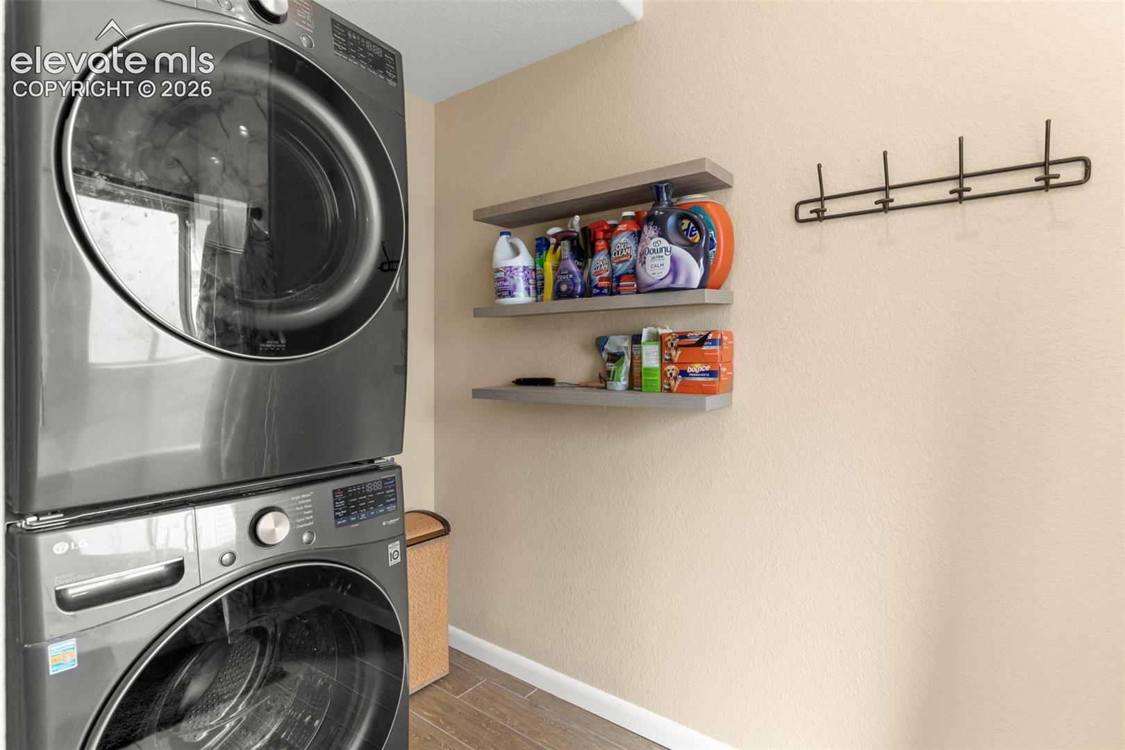 Stacked high-capacity laundry appliances featuring a metallic finish, complemented by three wall-mounted floating shelves and a horizontal metal wall hook rack
