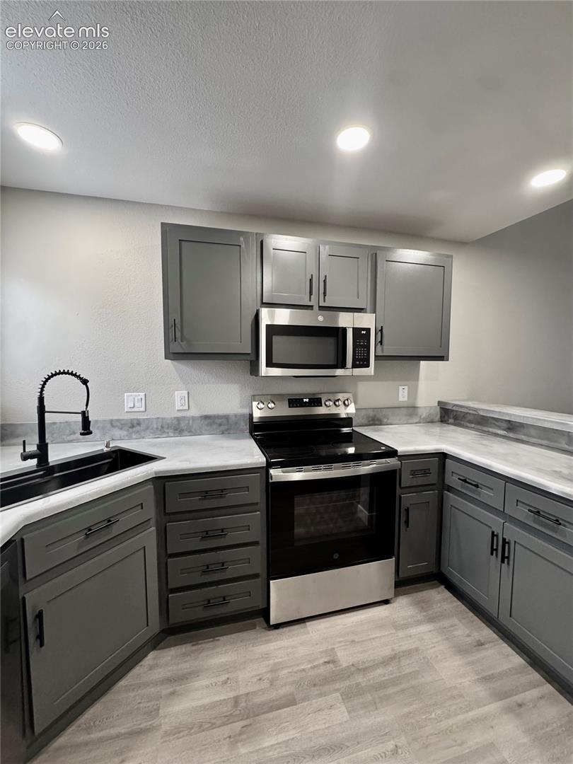 Kitchen featuring gray cabinetry with black hardware, stainless steel appliances, a black sink with a matte black faucet, and wood-finish flooring