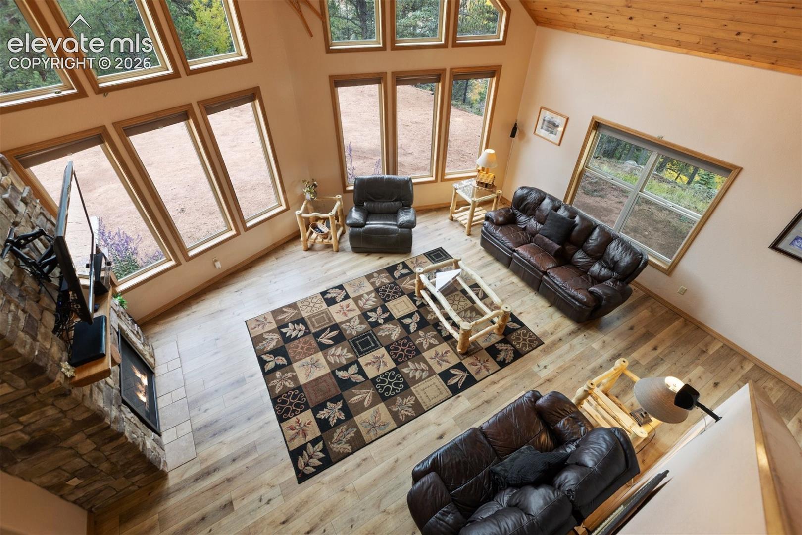 Vaulted wood-paneled ceiling, stone-clad fireplace, wood-finish flooring, and multiple large windows