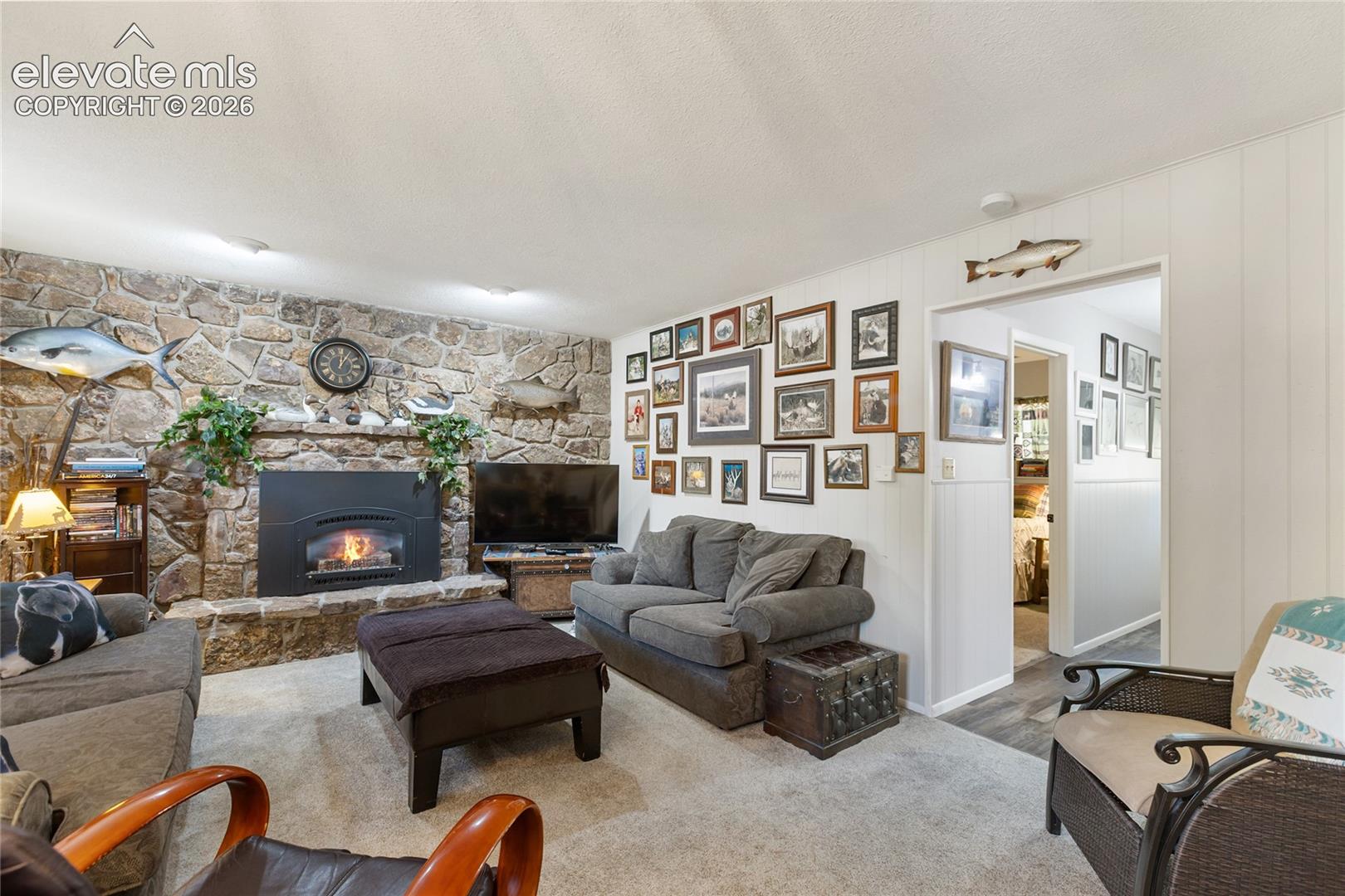 Stone-clad fireplace with a hearth, wall-mounted light fixtures, and light-toned flooring