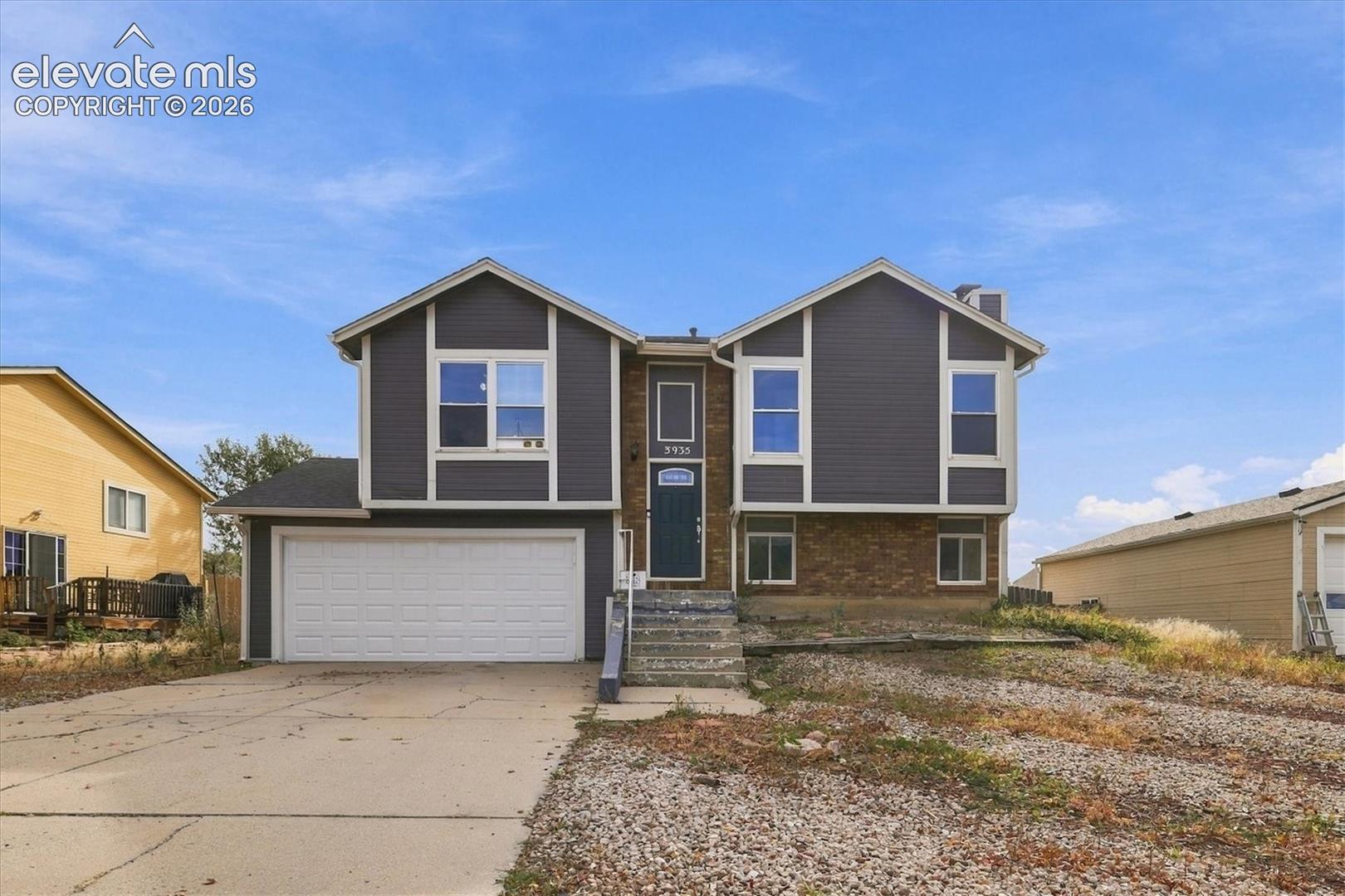 Split-level exterior featuring dark gray siding, brick veneer accents, a double-car garage, and concrete driveway