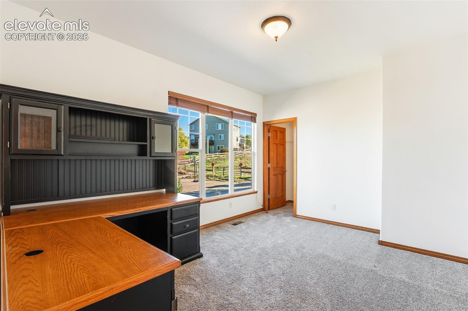 Room featuring neutral wall-to-wall carpeting, multi-pane window with wood-trim, six-panel wood door, and overhead light fixture