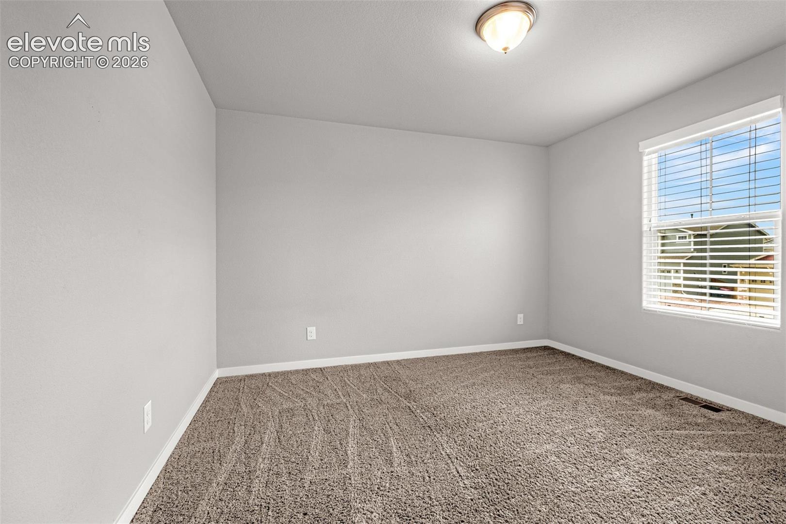 Textured carpet flooring, neutral paint palette, flush mount ceiling light, and window with blinds
