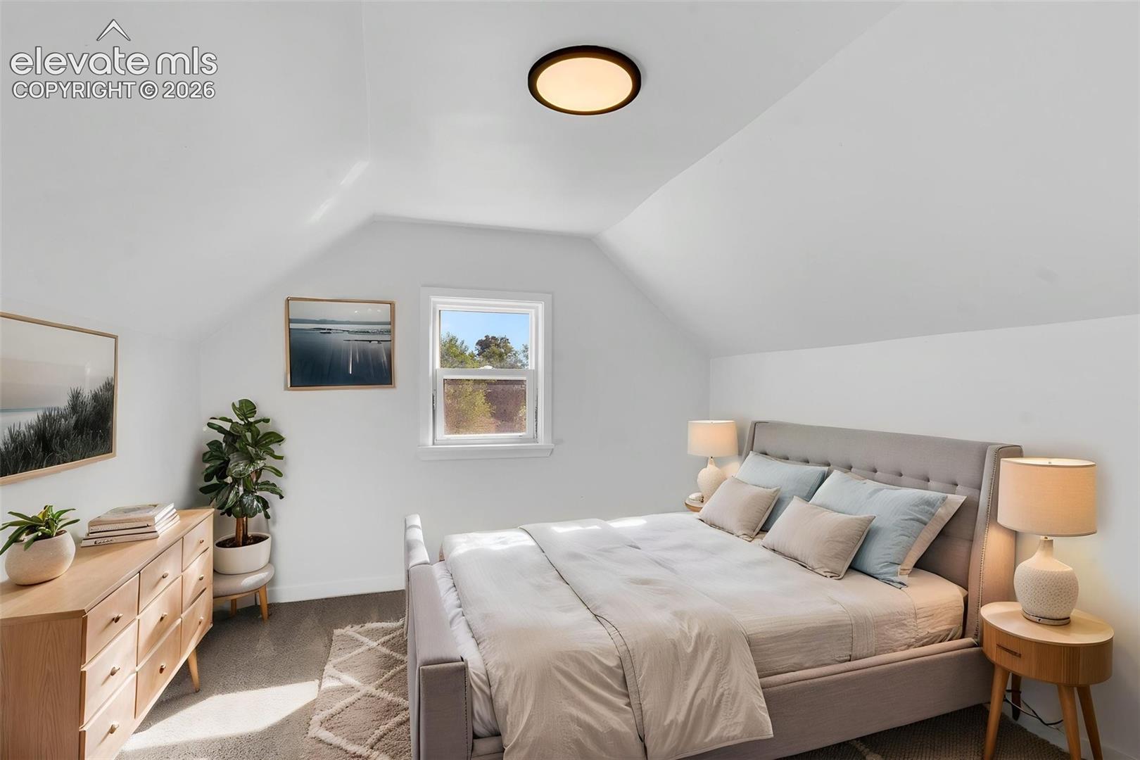 Vaulted ceilings with a neutral color palette, carpeted flooring, and a flush-mount circular lighting fixture