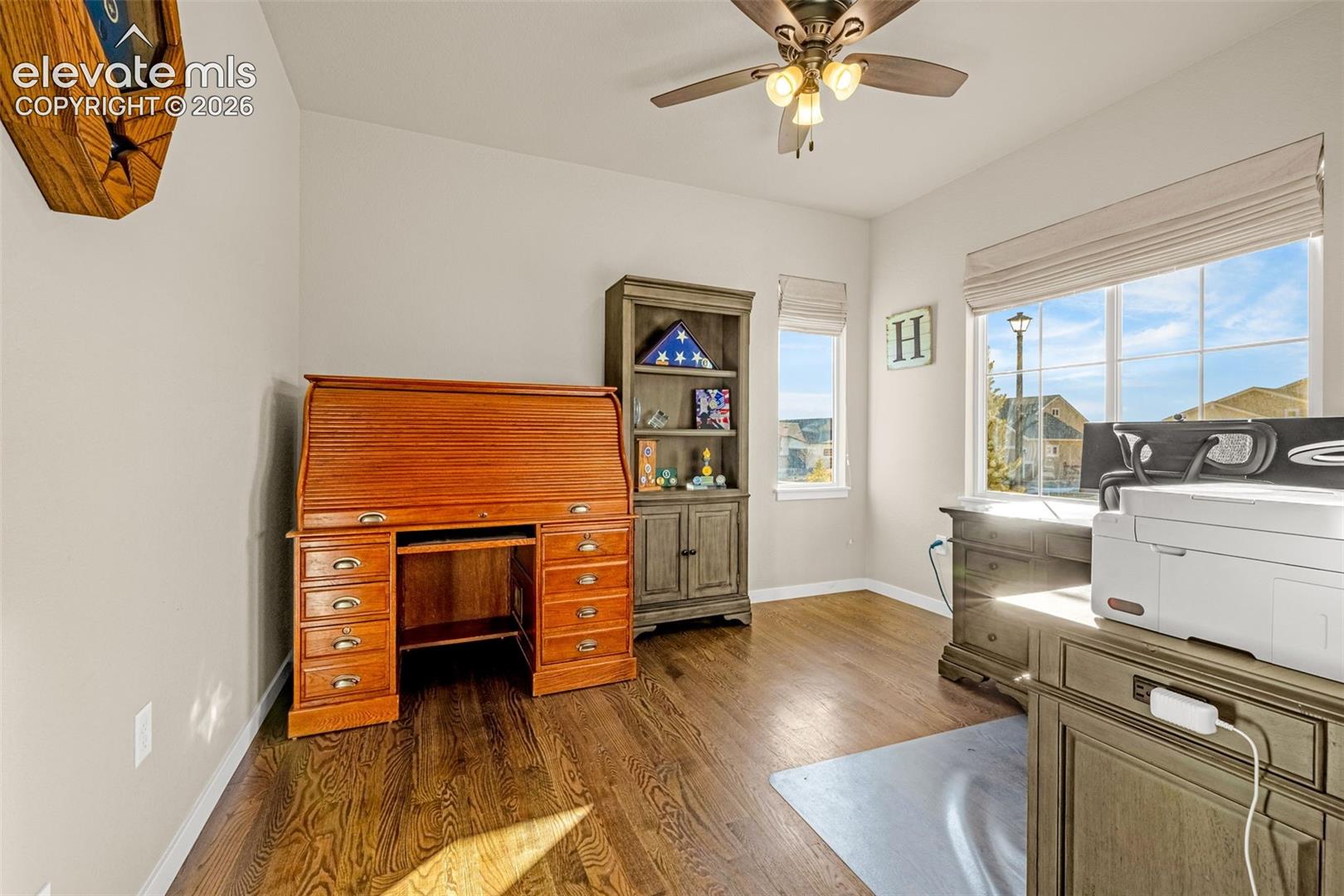 Wood-finish flooring, multi-pane windows with integrated shades, and a ceiling-mounted light fixture with a multi-blade fan