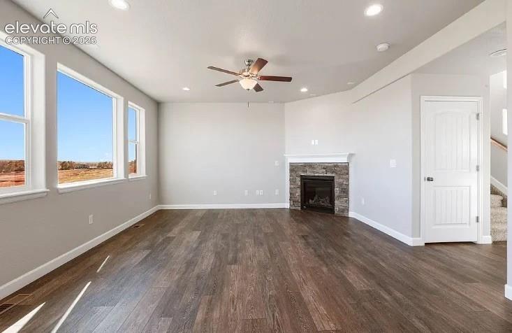 Open-concept interior featuring wood-finish flooring, a corner fireplace with a stone-texture surround, recessed lighting, and large windows