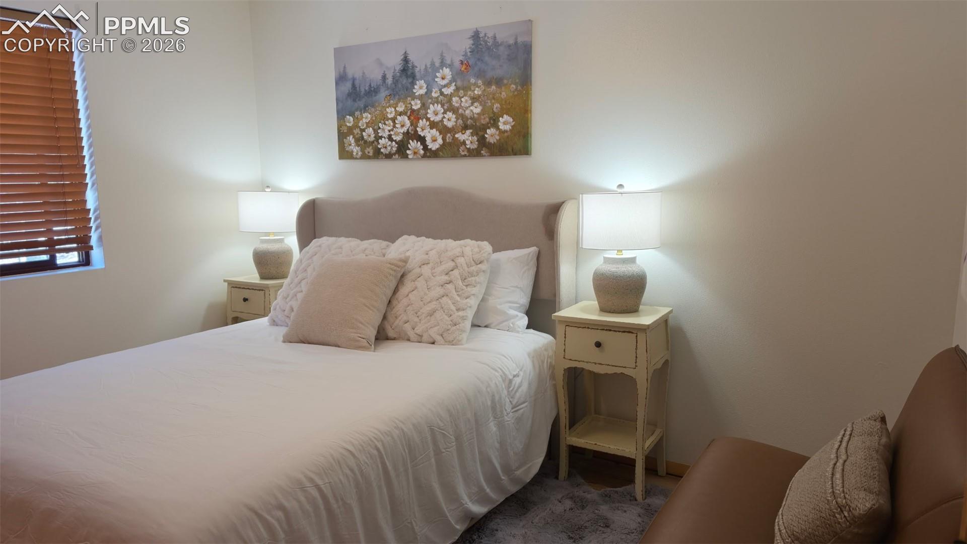 Room featuring neutral wall tones, a window with wood blinds, and a built-in upholstered headboard