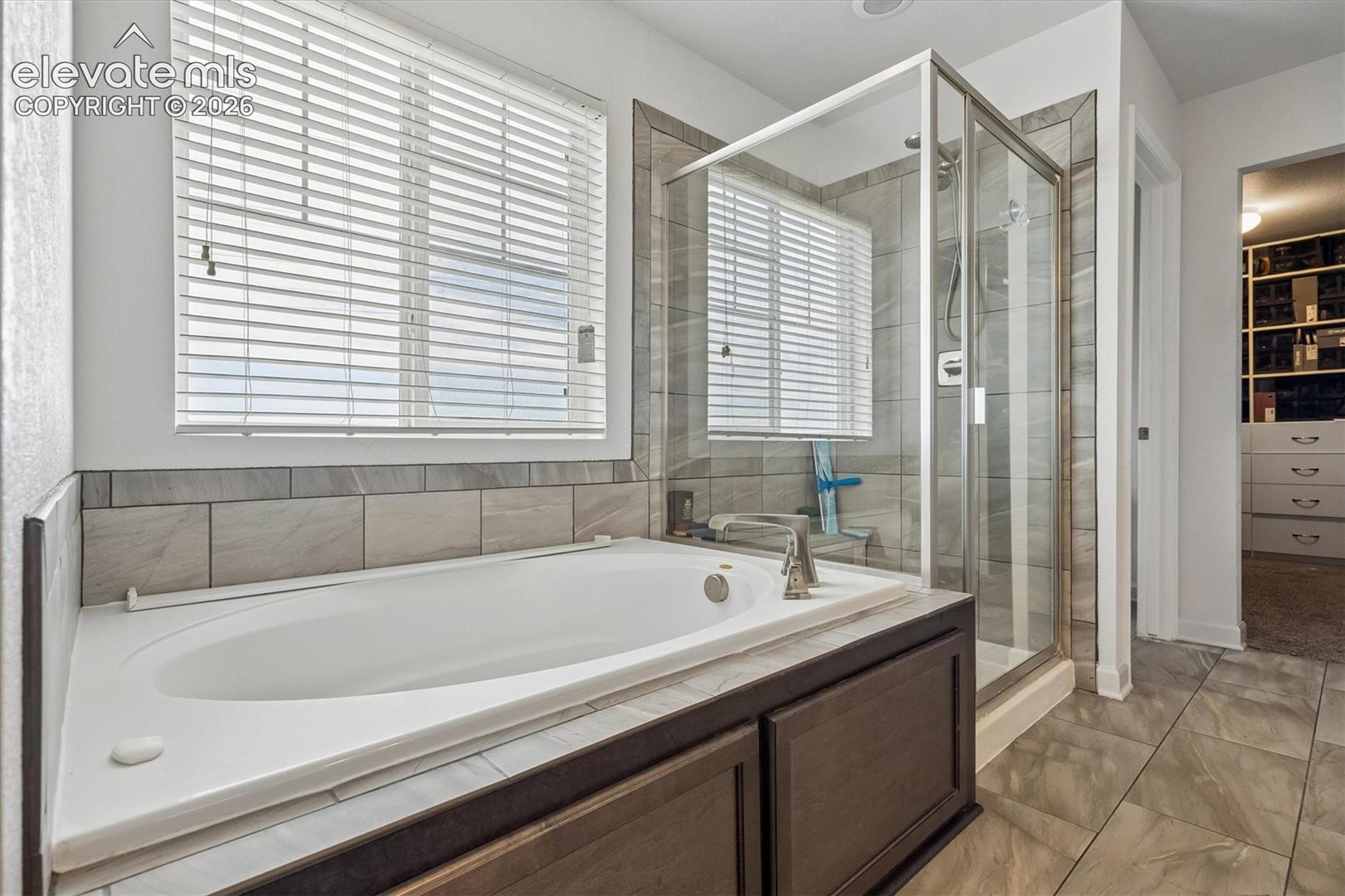 Soaking tub with a tile surround, separate glass-enclosed shower, and wood-finish cabinetry