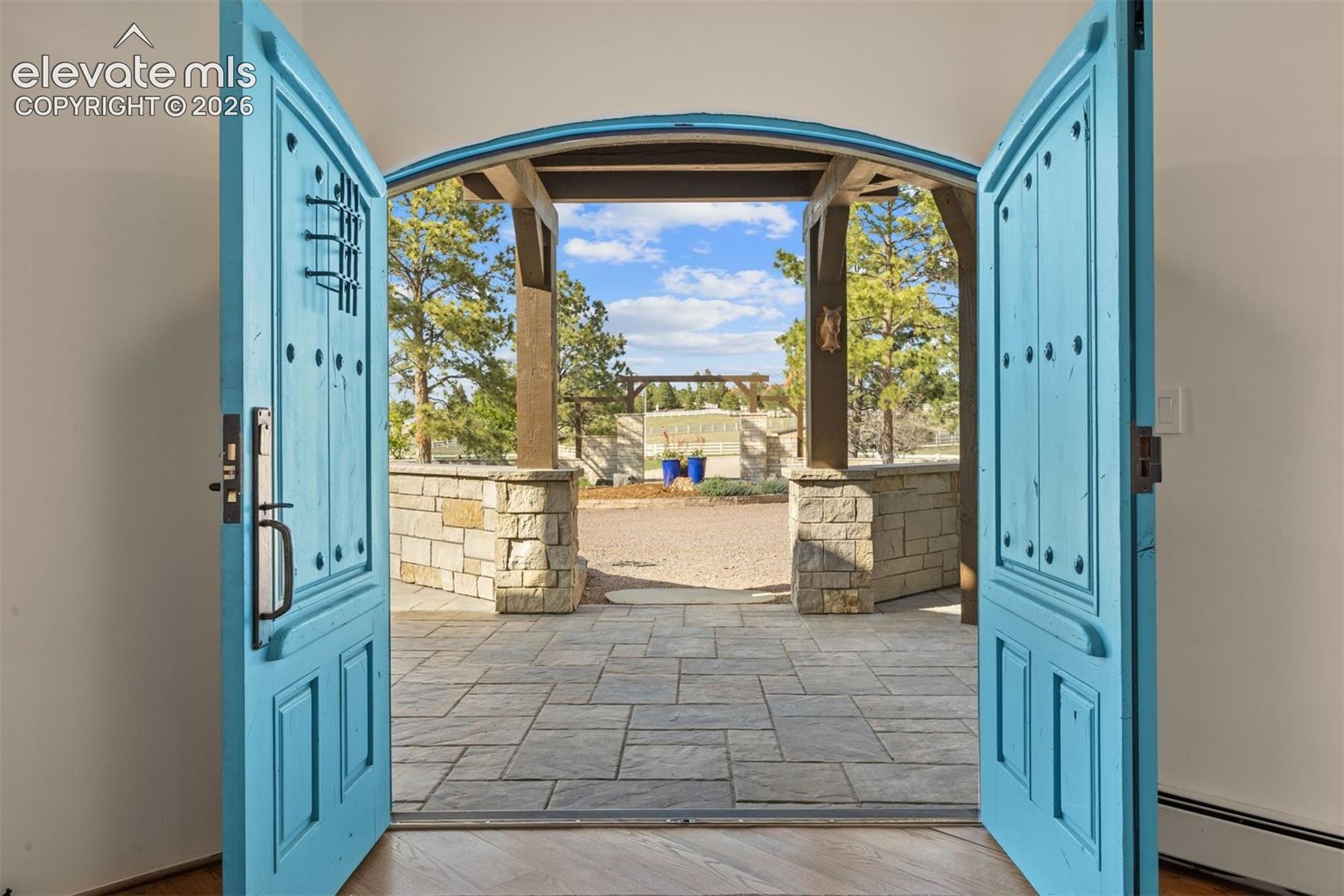 Custom double-arch solid wood entry doors commissioned from VML Custom Woodworks out of Corrales, NM, with hand-chiseled details, forged iron hardware, clavos nail head accents, and an interior peep window. 