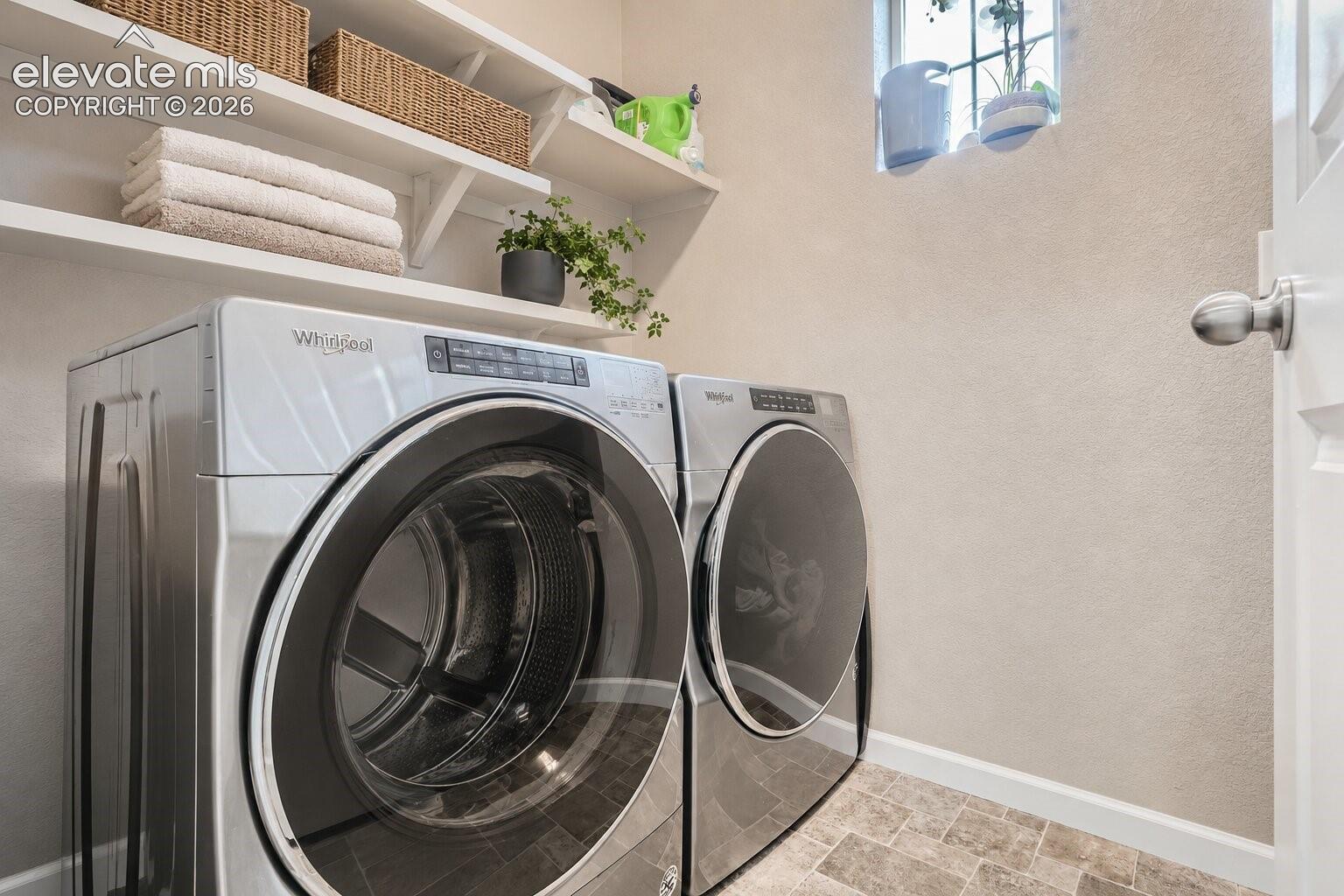Laundry space featuring built-in wall-mounted shelving and natural stone-finish tile flooring