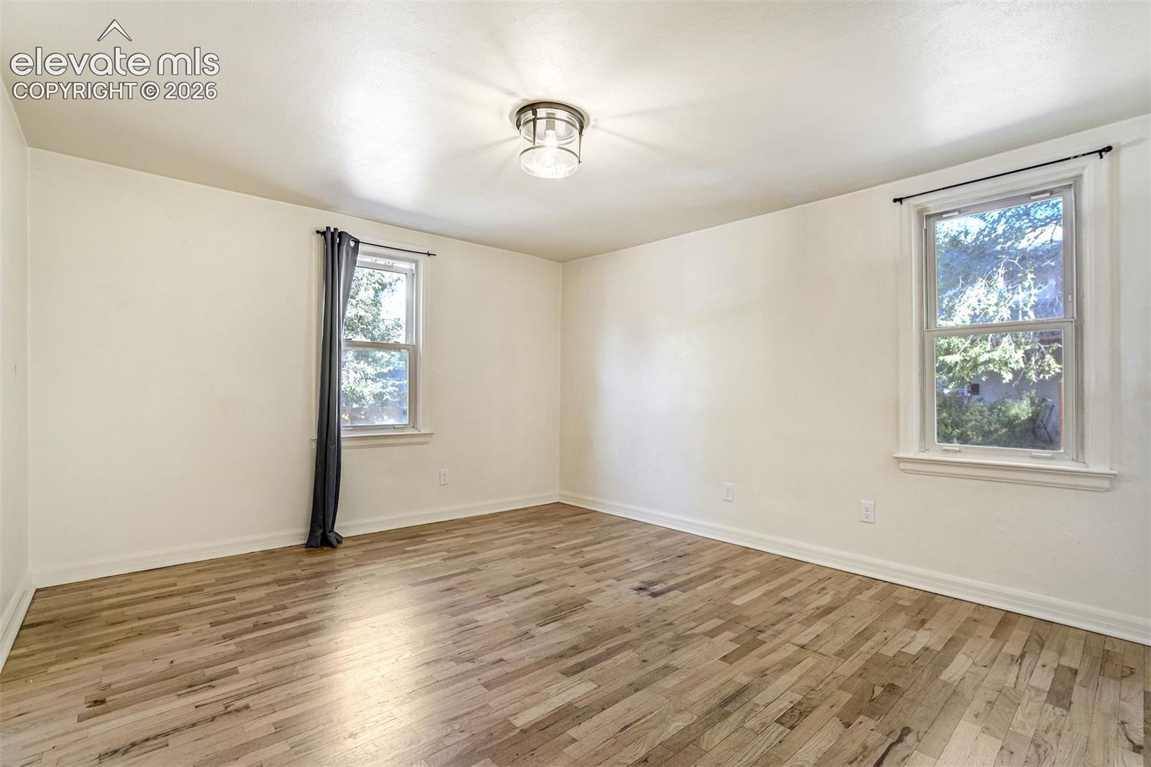 Room featuring wood-finish flooring, two double-hung windows, and a central ceiling-mounted light fixture