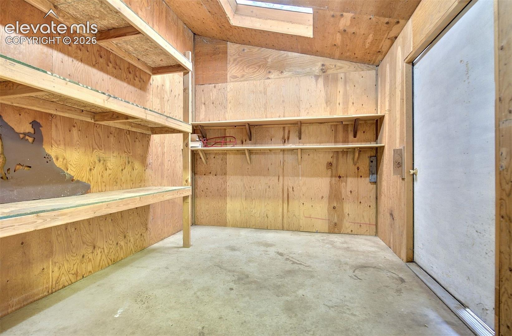 Storage space featuring plywood wall paneling, built-in wooden shelving units, concrete flooring, and a skylight