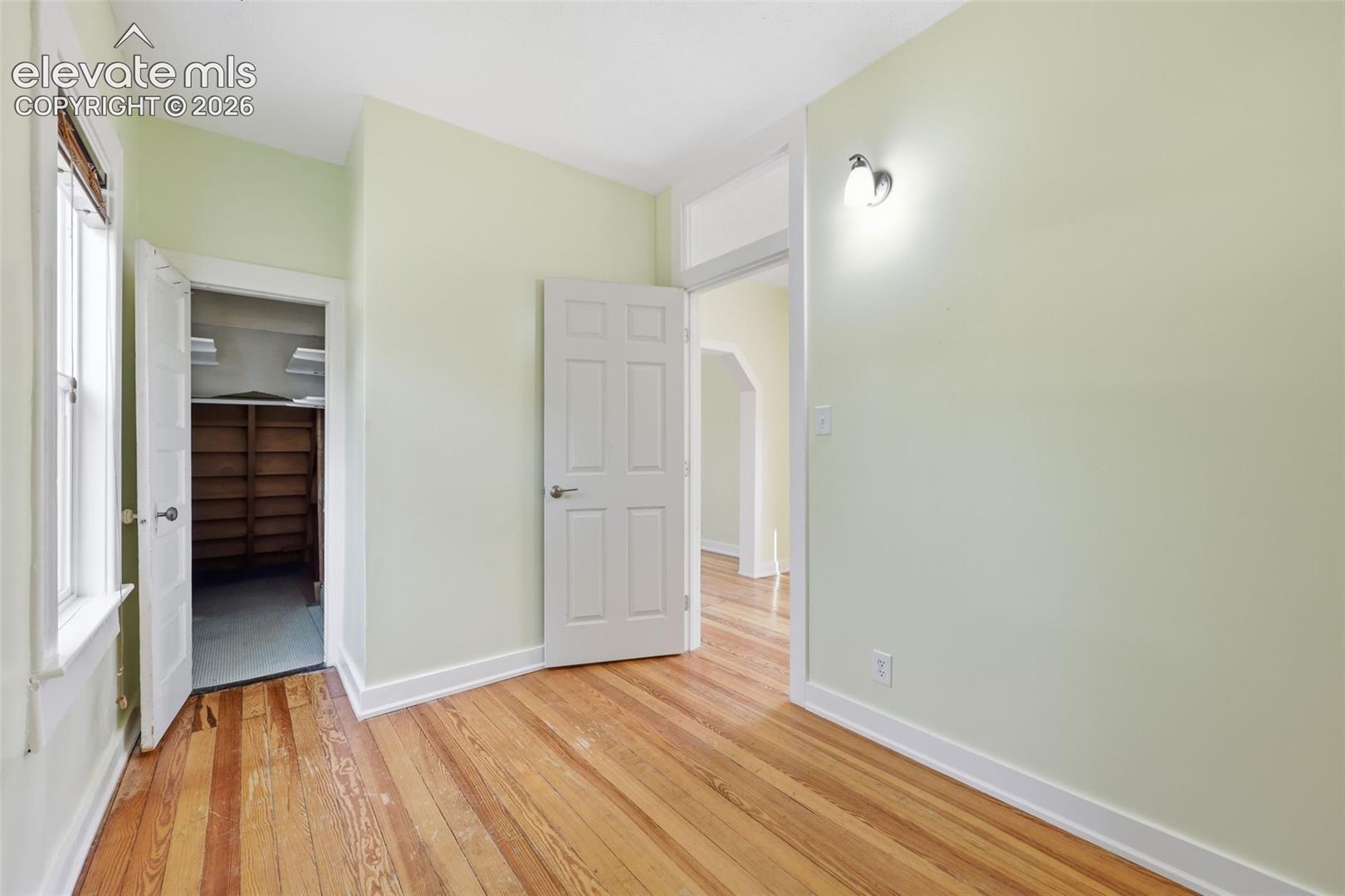 Main-floor bedroom with pine hardwood flooring throughout, walk-in closet, white trim, and a wall-mounted light fixture.