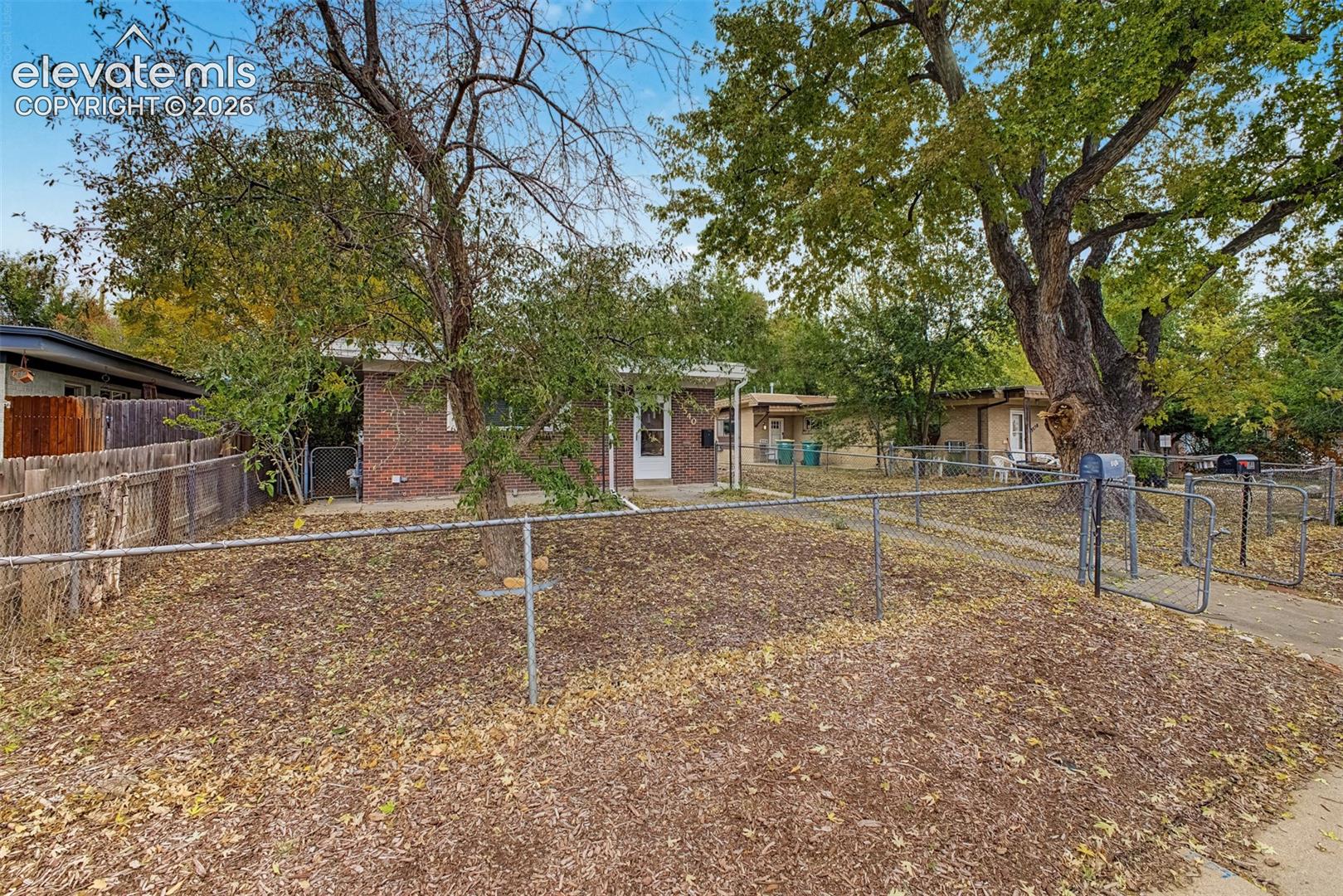 Single-story brick exterior featuring a chain-link fenced perimeter and mature trees