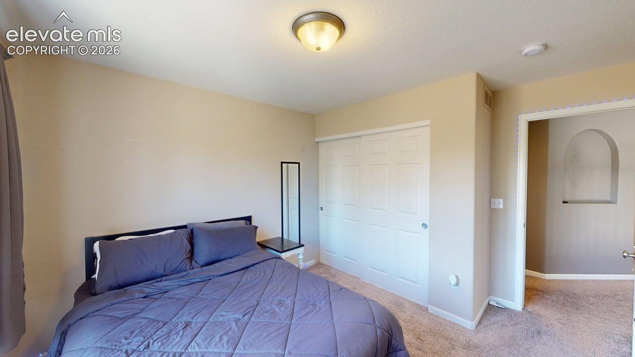 Room featuring neutral wall tones, textured carpeting, and a built-in closet with white sliding doors