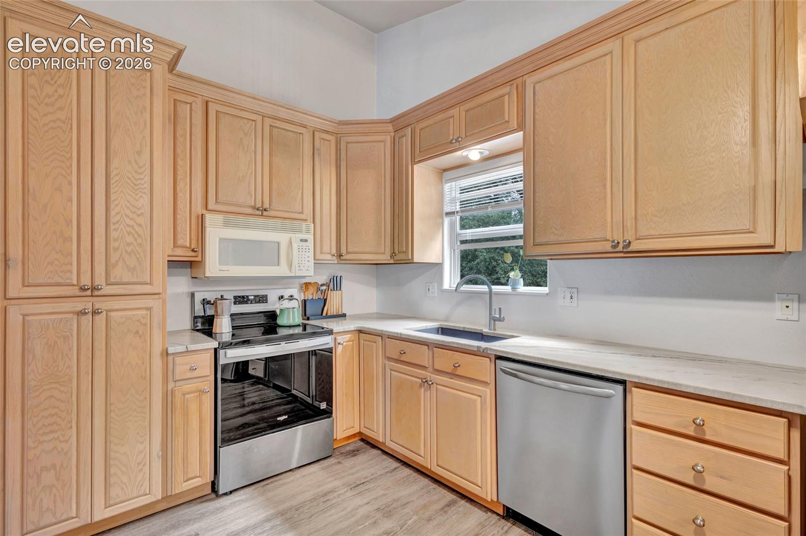 Kitchen featuring extensive light wood-finish cabinetry, stainless steel appliances, light-toned countertops, and wood-finish plank flooring