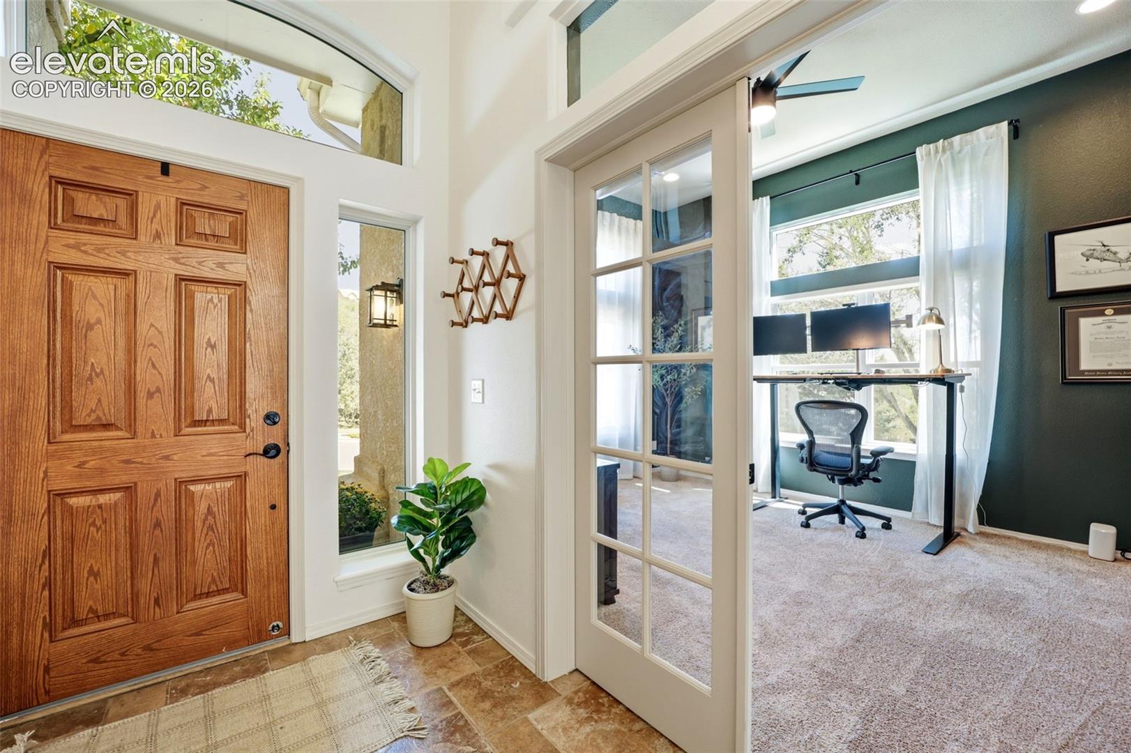 Solid wood entry door with transom window, side-light window, tile flooring, and an office with glass-paneled French doors