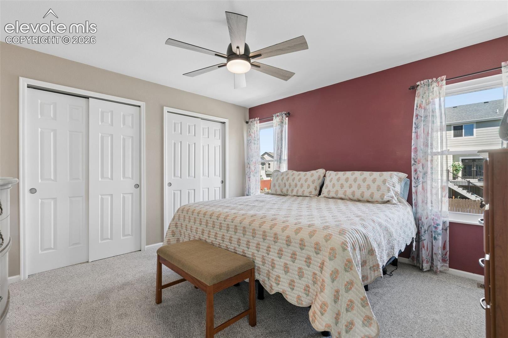 Recessed lighting, ceiling fan with light fixture, two windows, two sliding closet doors, and light-toned carpet flooring