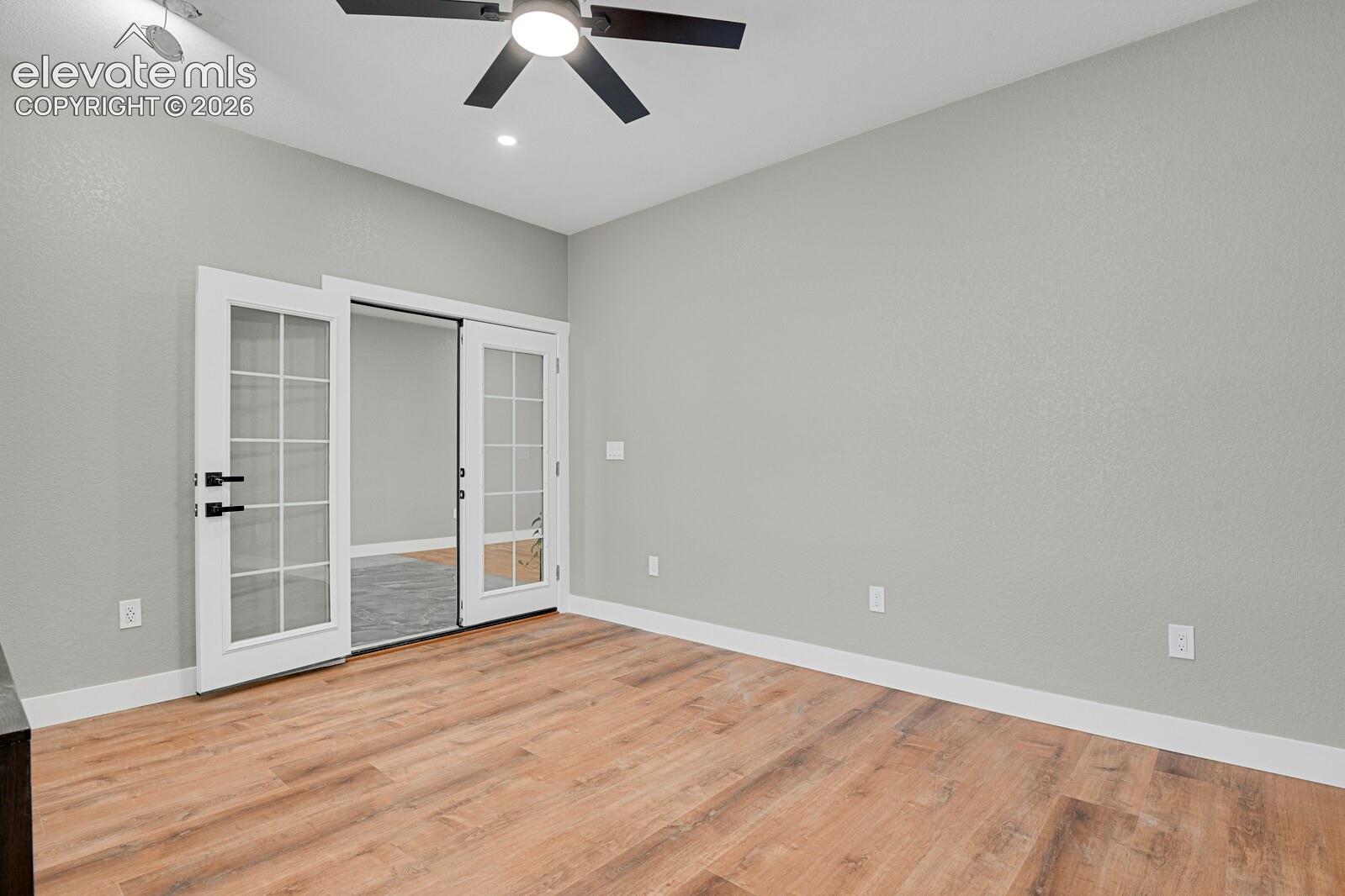 Room featuring wood-finish flooring, neutral wall paint, multi-pane glass French doors with matte black hardware, and a ceiling fan with integrated lighting