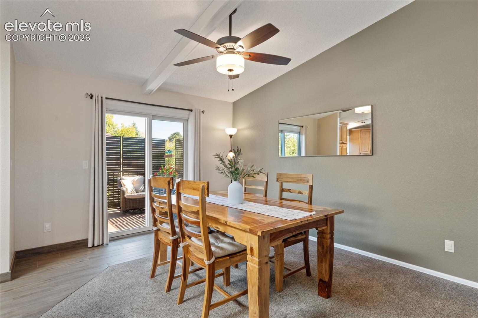 Dining area featuring vaulted ceilings, a central ceiling fan with integrated lighting, and a sliding glass door providing exterior access