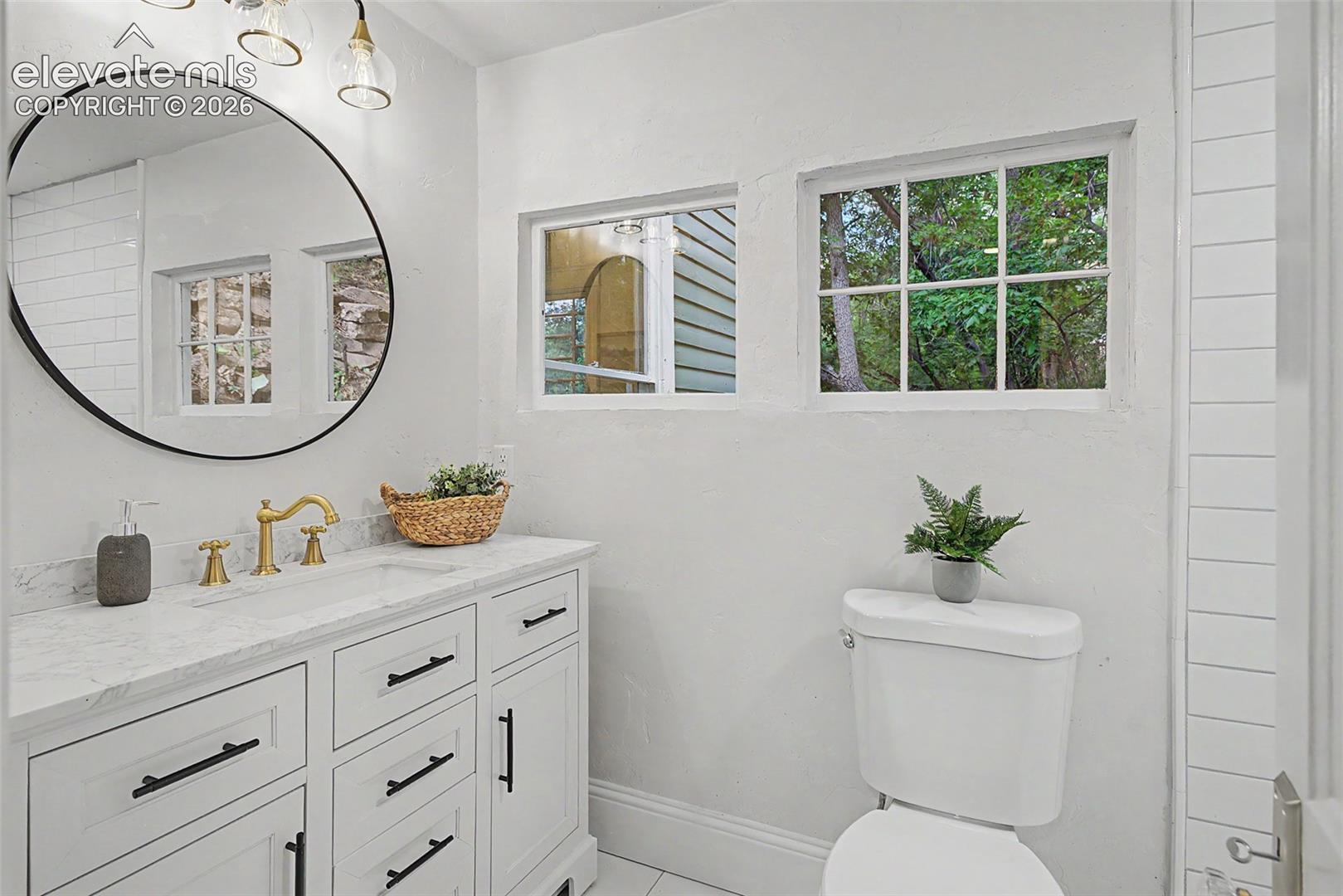 Bathroom featuring a white vanity with black hardware, a marble-finish countertop, and a round black-framed mirror