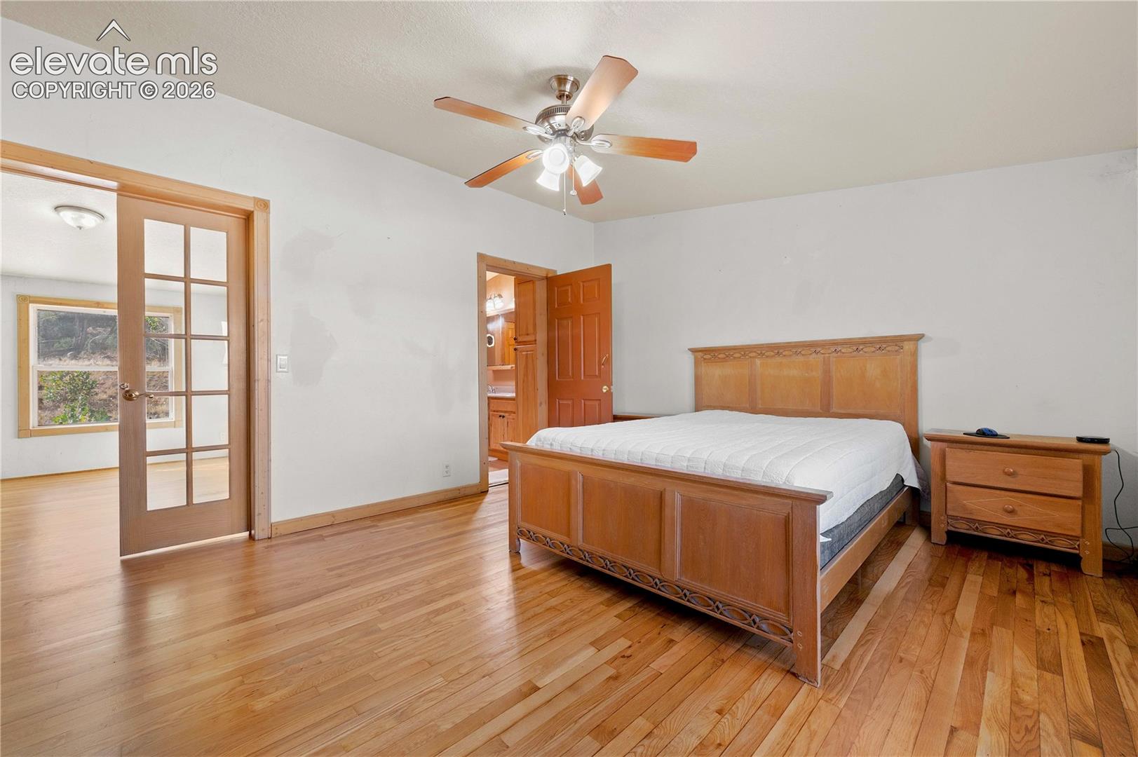 Bedroom featuring light hardwood / wood-style floors, french doors, ensuite bath, and ceiling fan