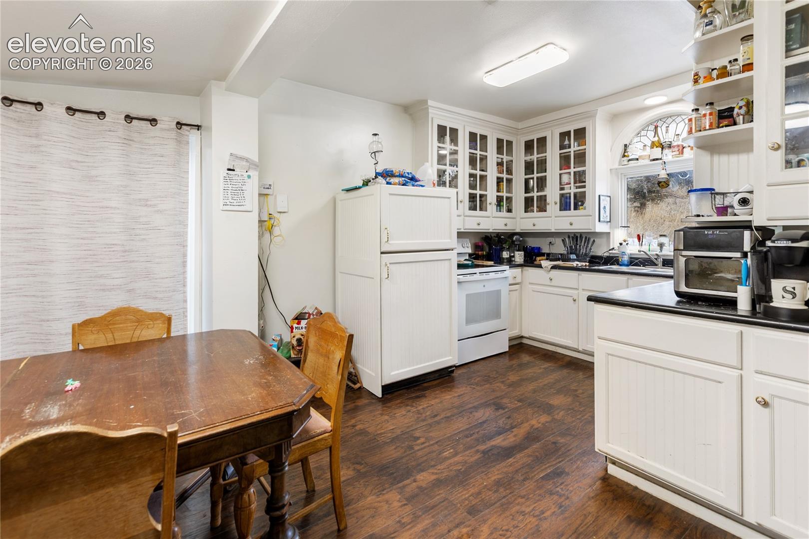 Kitchen featuring wood-finish flooring, white cabinetry with glass-front uppers, beadboard detailing, and a prominent arched window