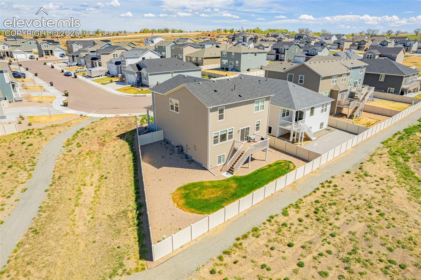 Two-story residence with a neutral exterior, featuring a private fenced yard and an elevated deck with stairs to grade