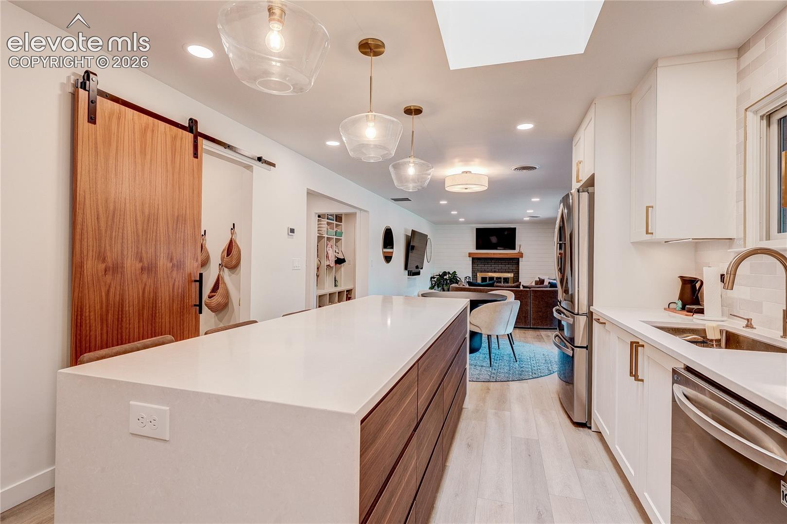 Kitchen island with waterfall countertop, stainless steel appliances, white cabinetry, and wood-finish flooring
