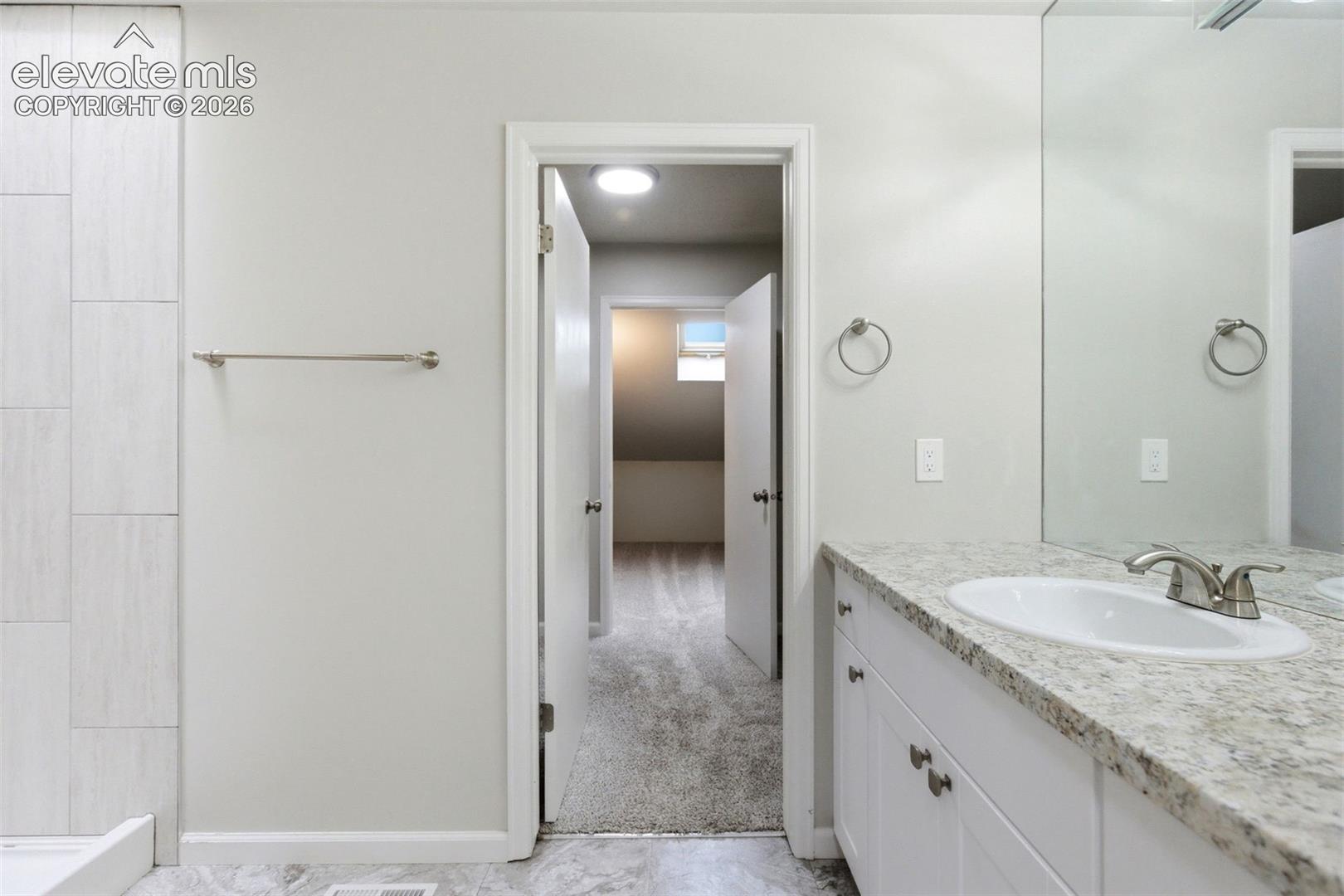 Bathroom vanity featuring a granite countertop, undermount sink, brushed nickel faucet, and white cabinetry with brushed nickel hardware