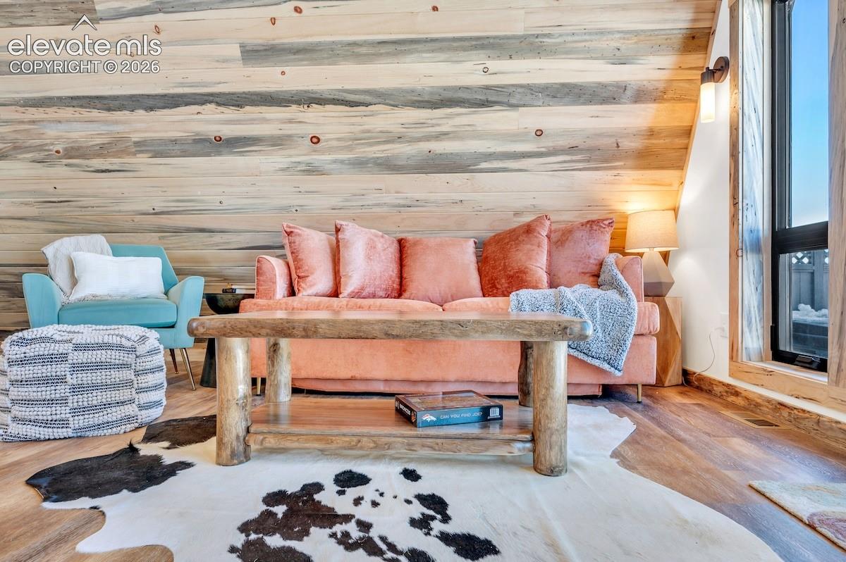 Vaulted ceiling with horizontal wood-plank paneling, wood-finish flooring, and wall-mounted sconce lighting