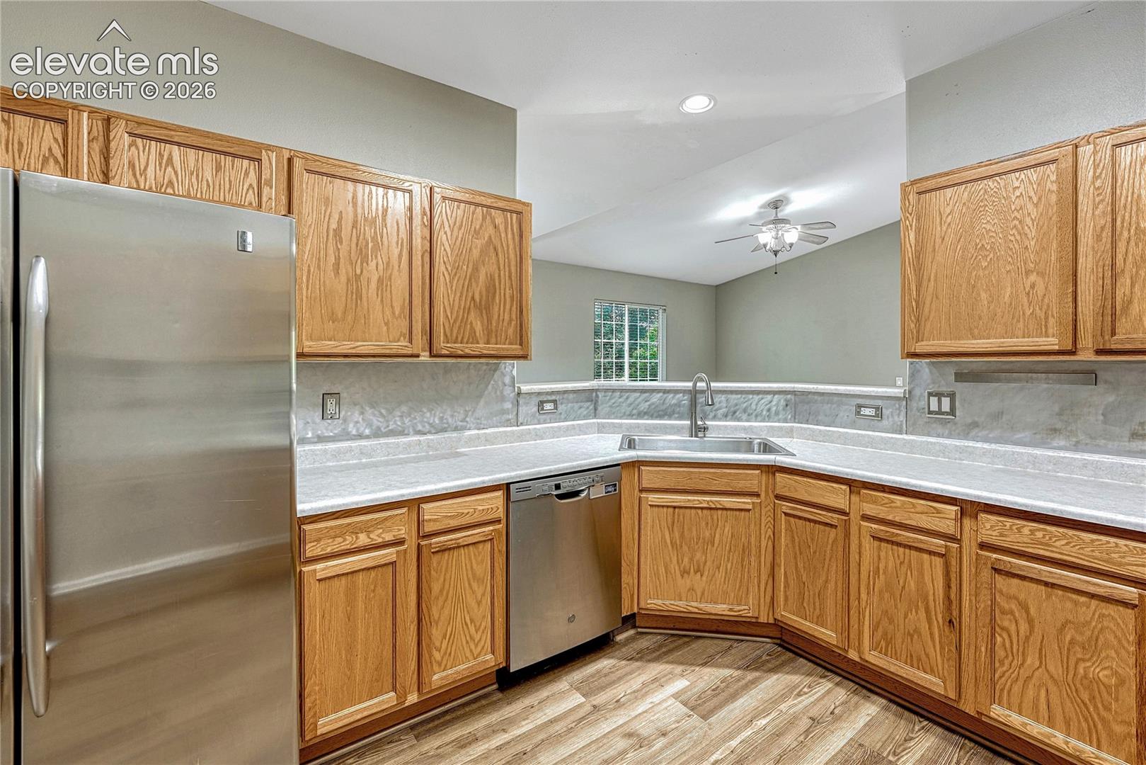 Kitchen featuring wood cabinetry, stainless steel appliances, neutral countertops, stone-texture backsplash, and wood-finish flooring