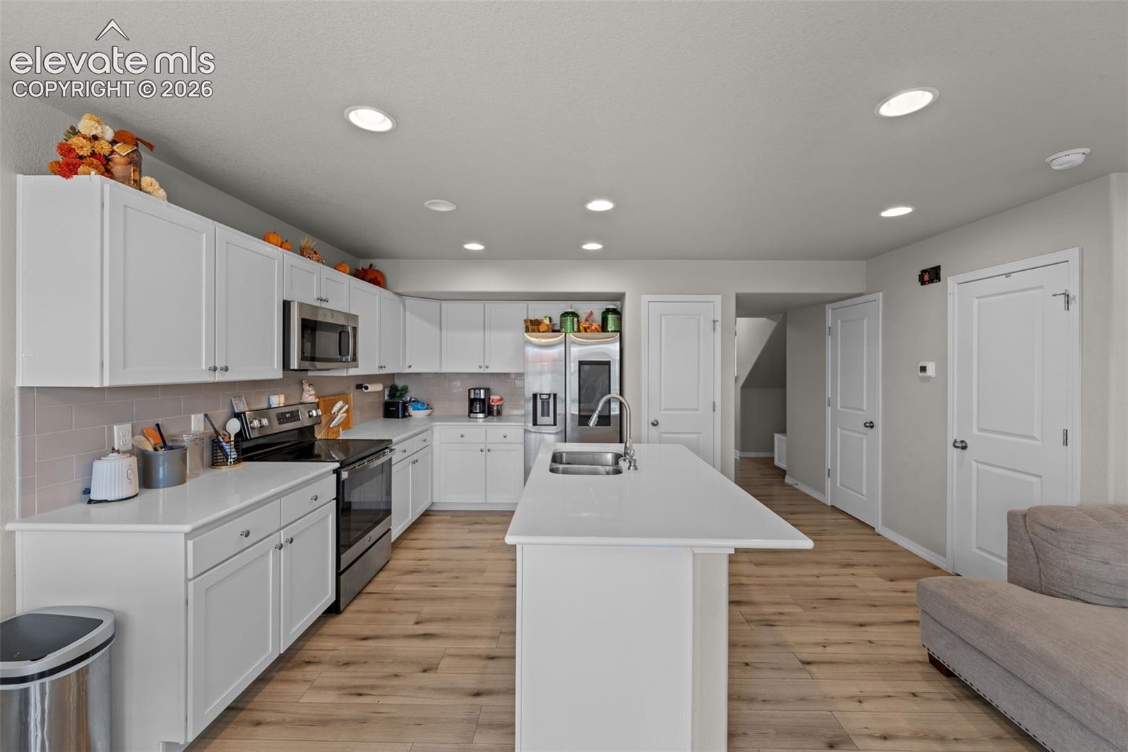 Kitchen featuring white shaker cabinetry, stainless steel appliances, a center island with sink, recessed lighting, and wood-finish flooring