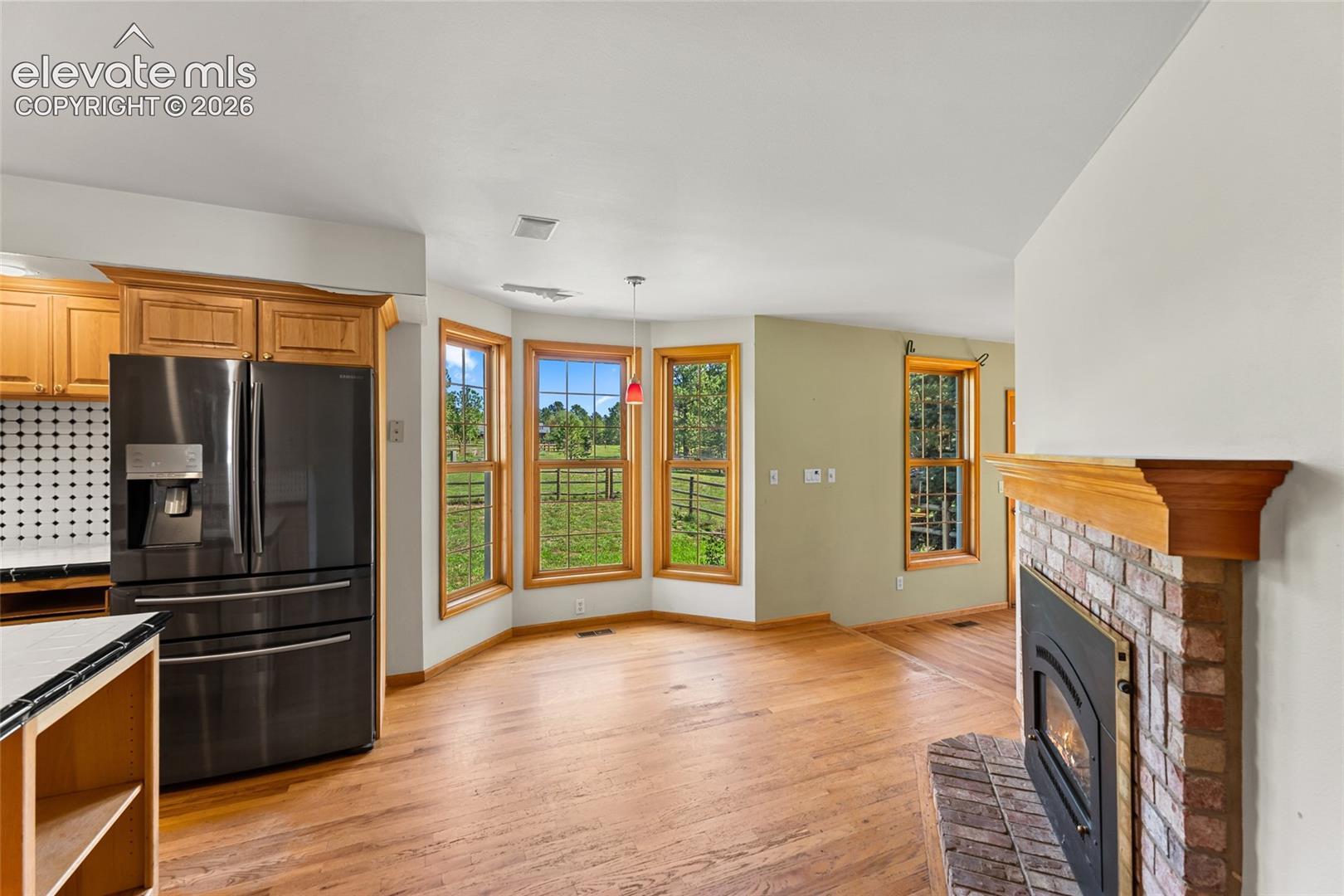 Hardwood flooring throughout, brick fireplace with wood mantel, kitchen cabinetry with built-in refrigerator, and bay windows