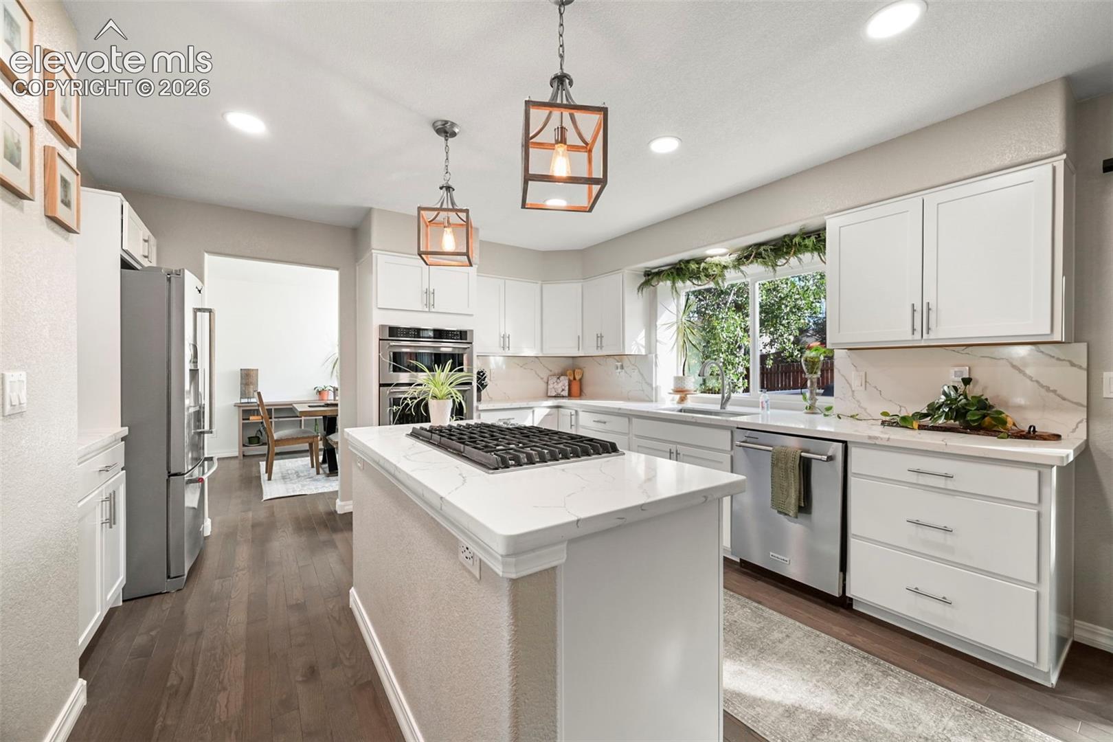 Gourmet kitchen featuring a center island with cooktop, stainless steel appliances, white cabinetry, quartz countertops, and dark wood-finish flooring