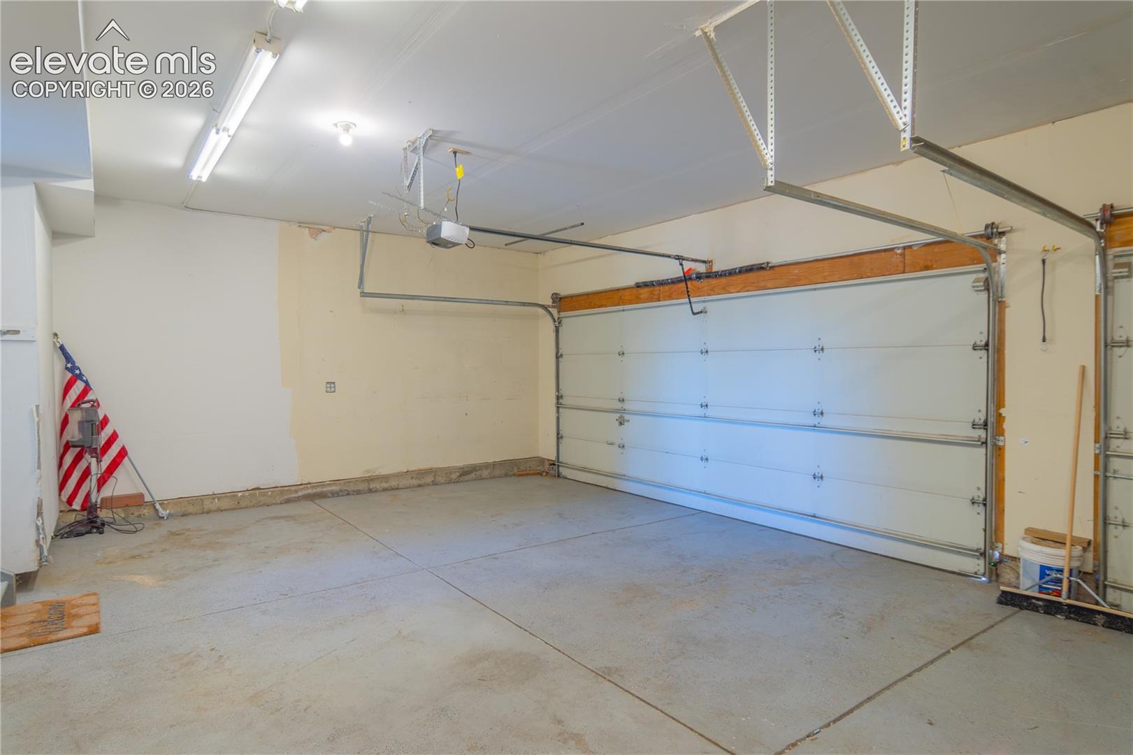Three-car garage with concrete flooring, overhead lighting, and room for vehicles and storage.