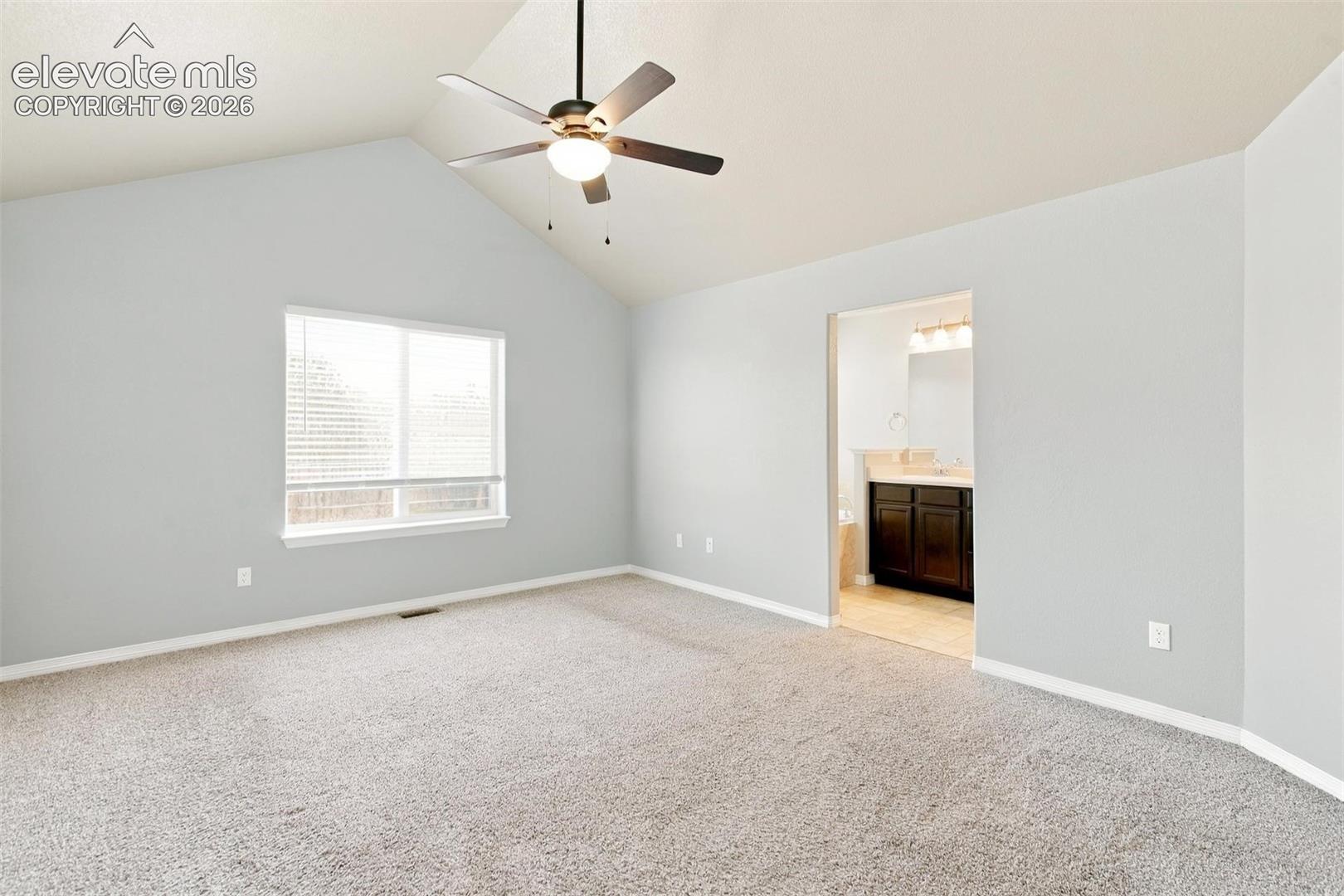 Vaulted ceilings featuring a central ceiling fan with integrated lighting, wall-to-wall carpeting, and a multi-pane window