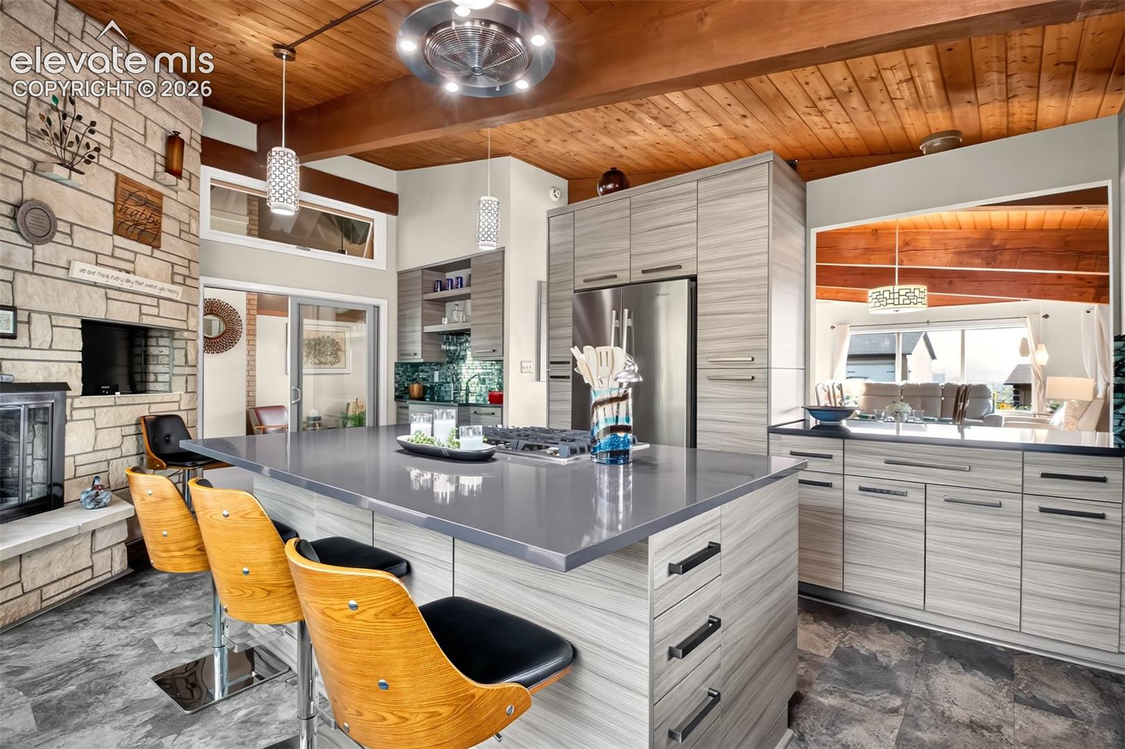 A view of the kitchen showing the breakfast bar island, the pass through to the dining room and a view of the stone gas fireplace