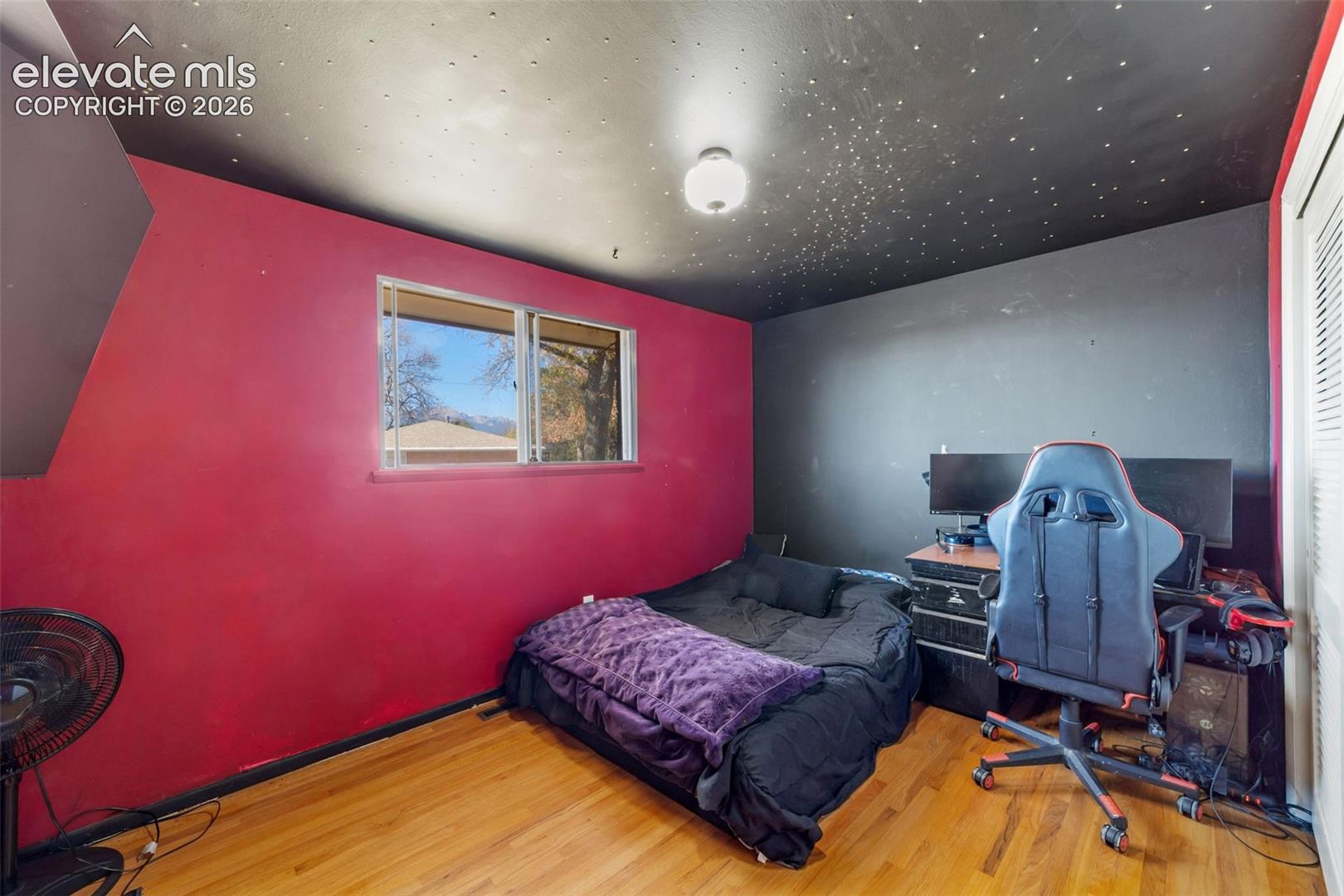 Room featuring wood-finish flooring, a window with exterior scenery, a black ceiling with integrated lighting, and a white bi-fold closet door
