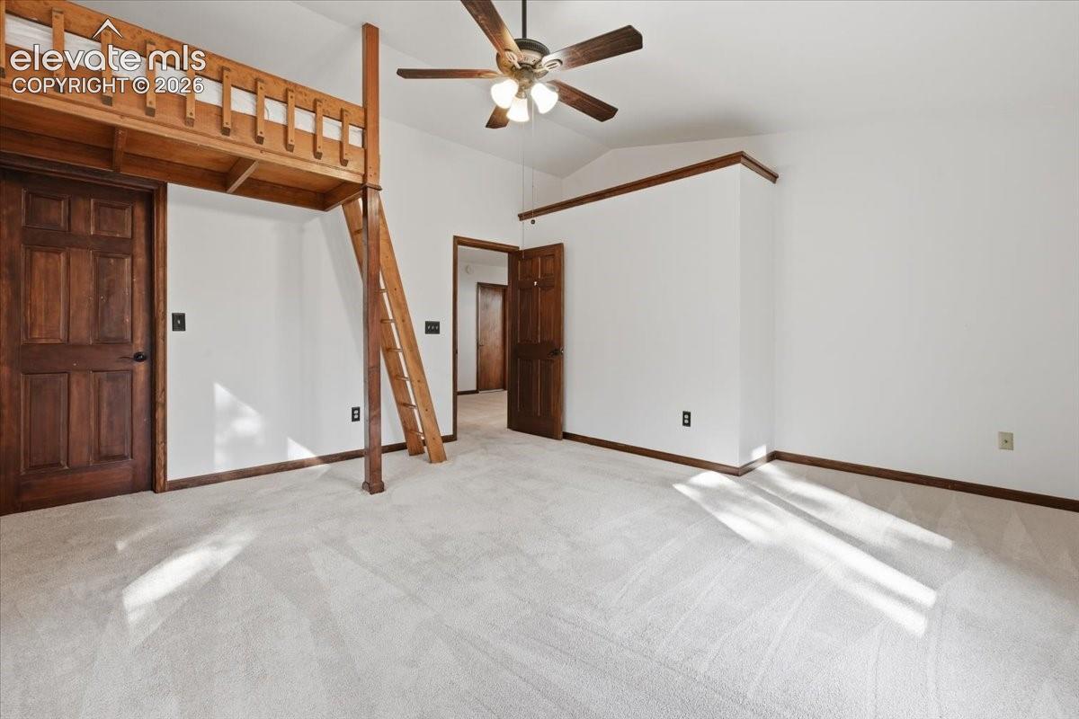Lofted bunk bed structure, vaulted ceiling, ceiling fan with light fixture, light-toned carpeting, and wood-paneled doors