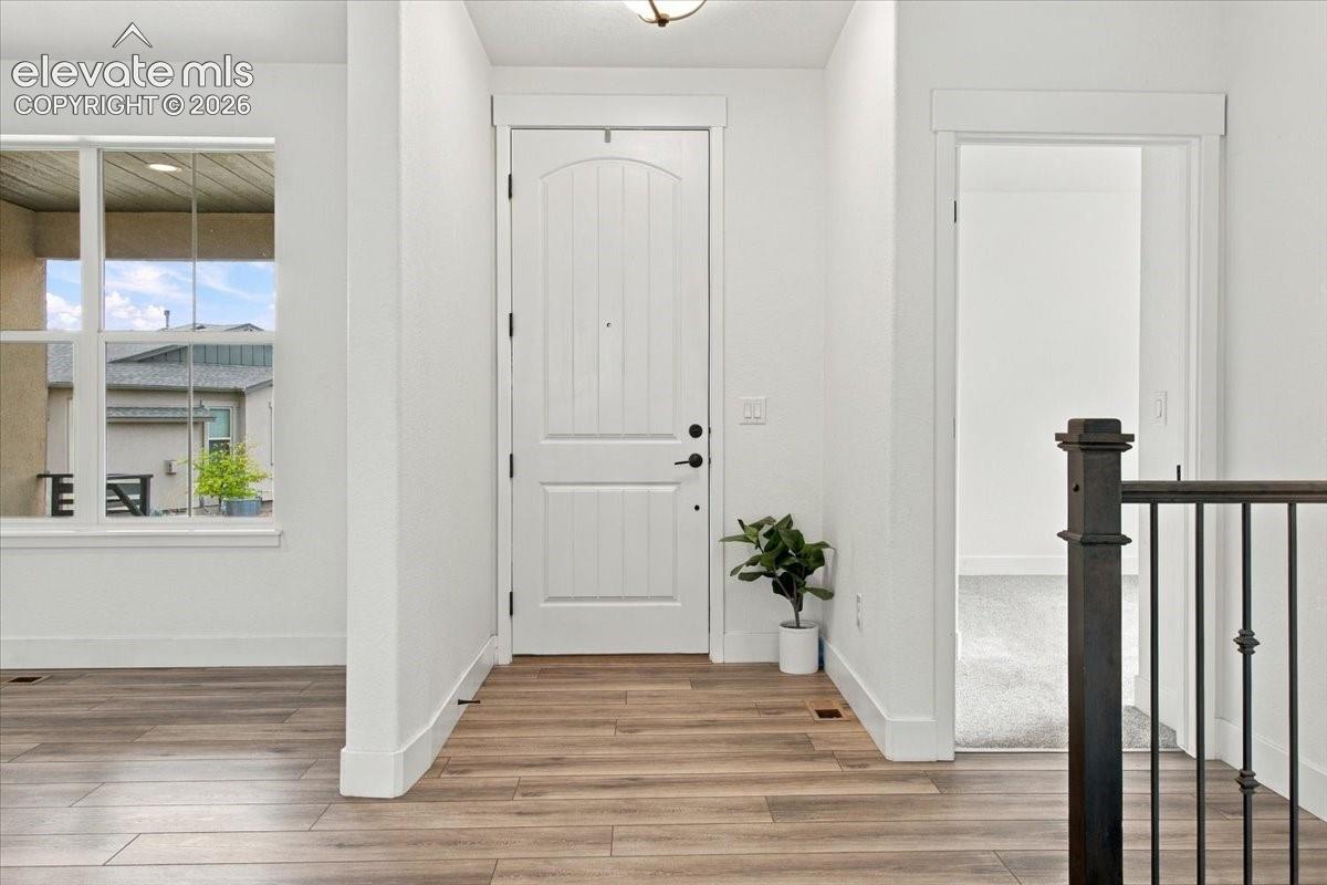 Entryway featuring an arched-panel door, wood-finish flooring, and a metal-spindle staircase railing