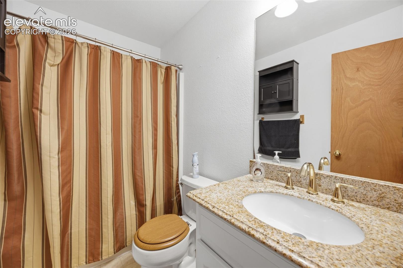 Bathroom vanity featuring a polished granite countertop, undermount sink, and brass-finish fixtures