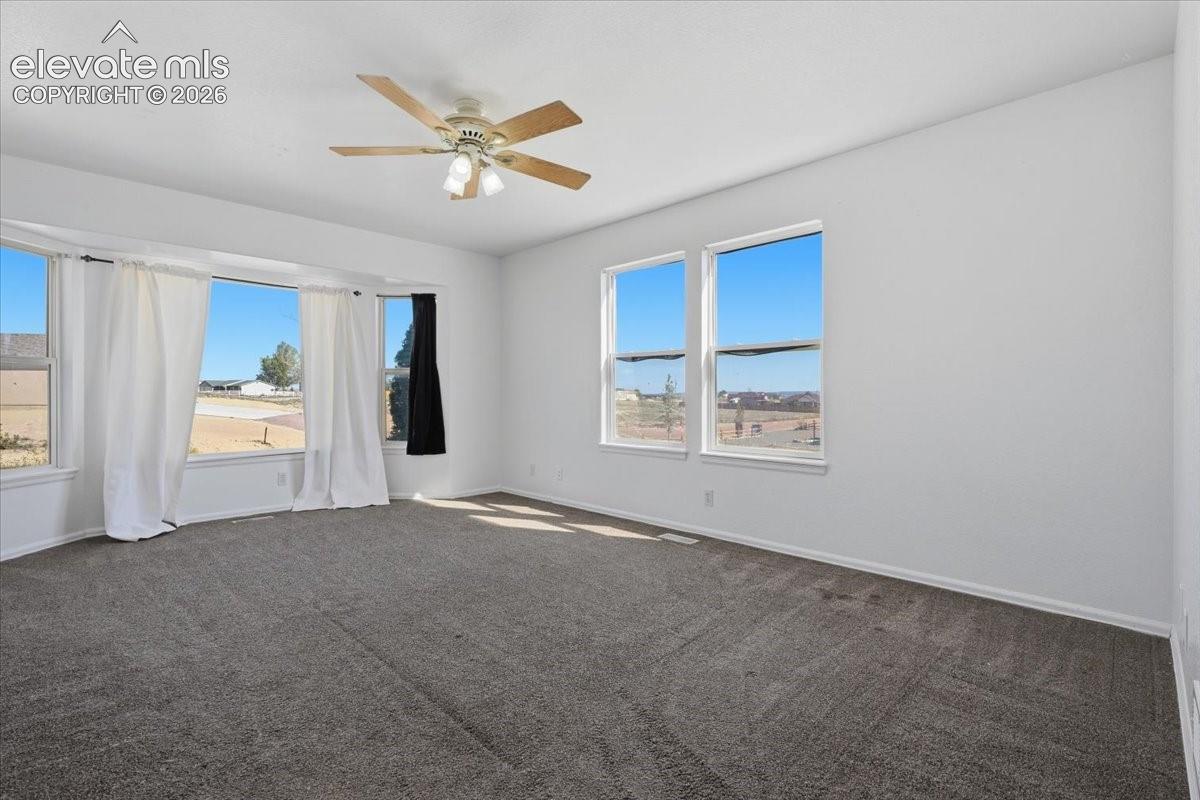 Spacious interior featuring a bay window, wall-to-wall carpeting, multiple double-pane windows, and a central ceiling fan with integrated lighting
