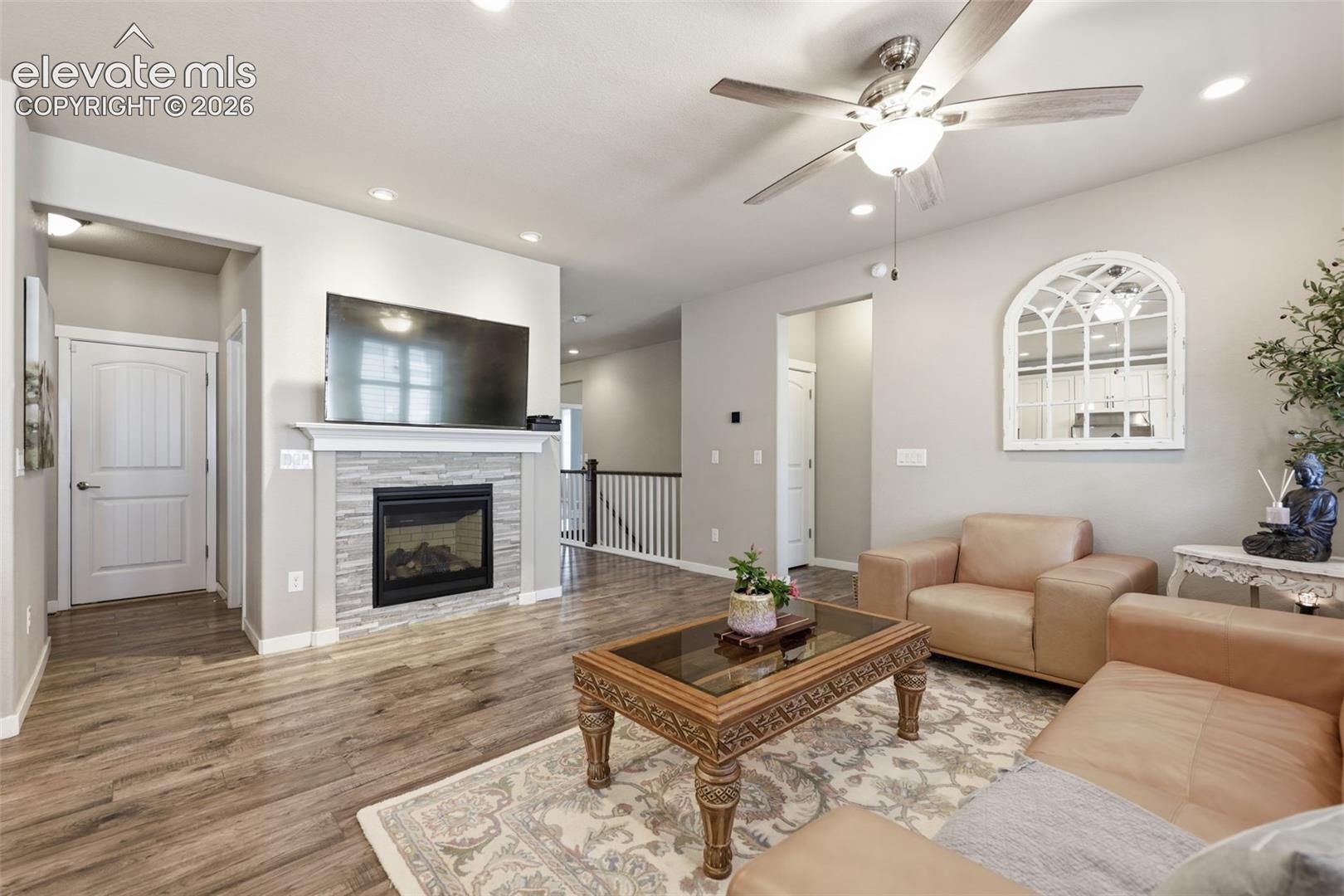 Light brown luxury vinyl plank flooring, recessed lighting, ceiling fan, contemporary fireplace with stone surround, and white balusters.