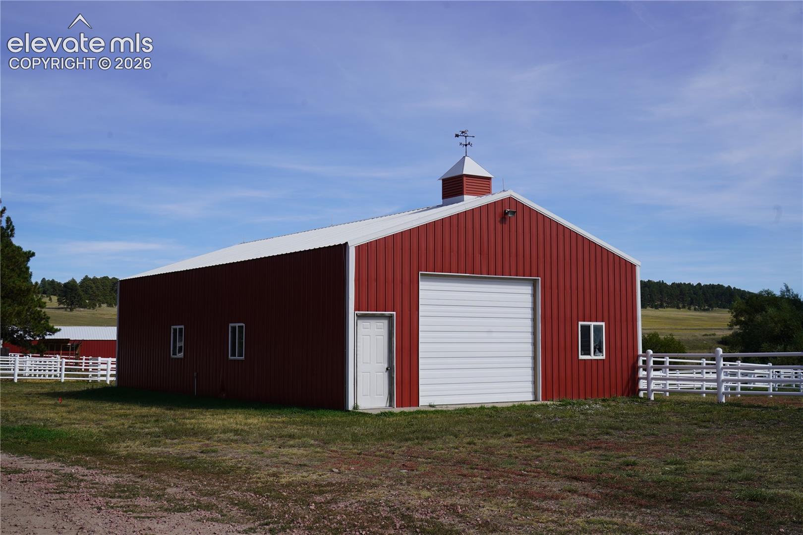 Red metal-sided barn with a white roll-up garage door, white entry door, and white-framed windows