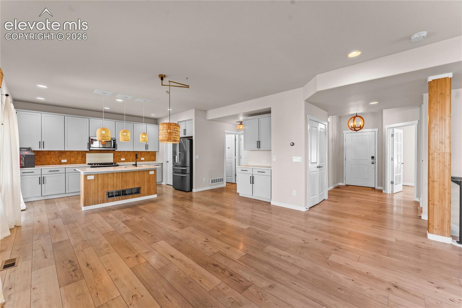 Open-concept kitchen featuring light-toned cabinetry, wood-finish flooring, a wood-paneled kitchen island, a textured backsplash, and hanging pendant lighting
