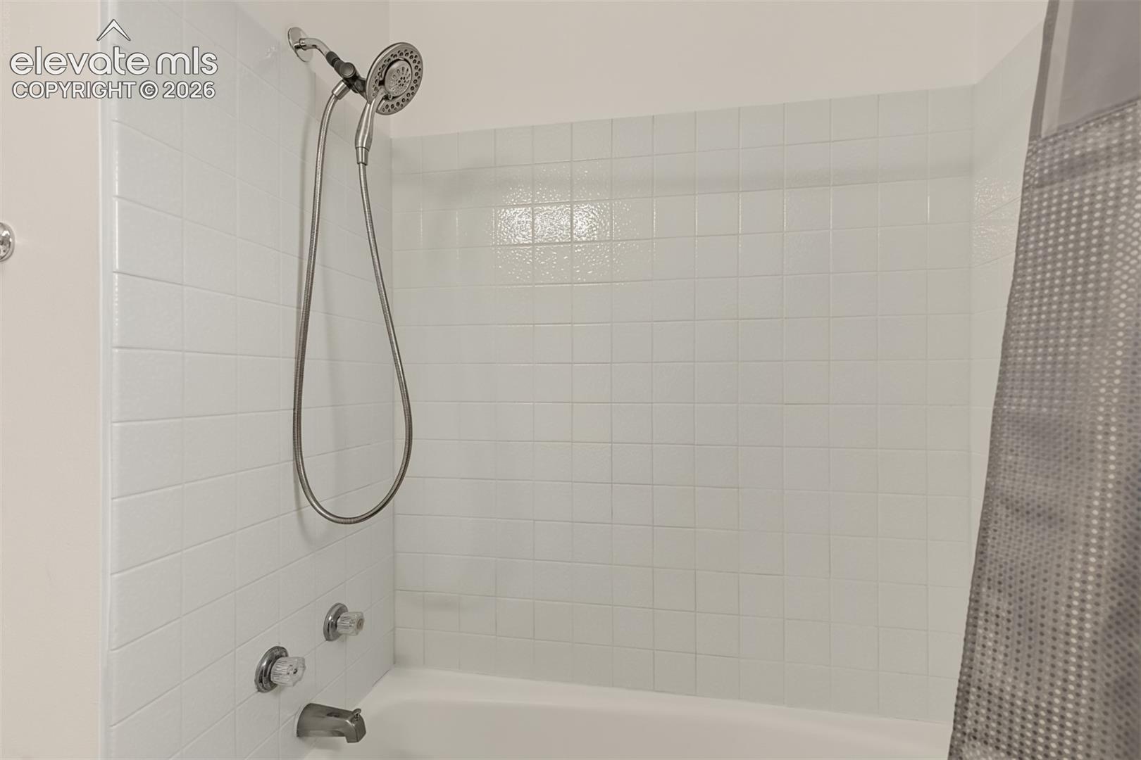 Shower and bathtub enclosure featuring white square tile surround, adjustable handheld shower head, and chrome plumbing fixtures