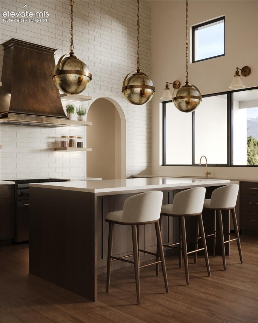 Kitchen featuring wood-finish flooring, a center island with a light-toned countertop, white subway tile backsplash, a metal range hood, and large windows