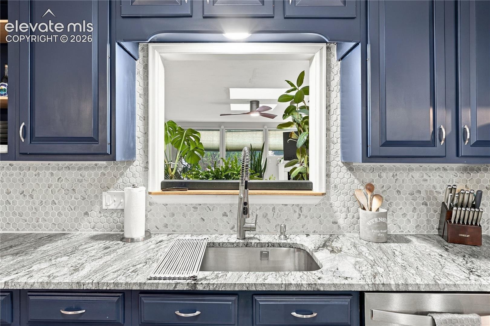 Kitchen area featuring navy cabinetry, stone-patterned countertops, a hexagonal tile backsplash, and an undermount stainless steel sink with a high-arch pull-down faucet