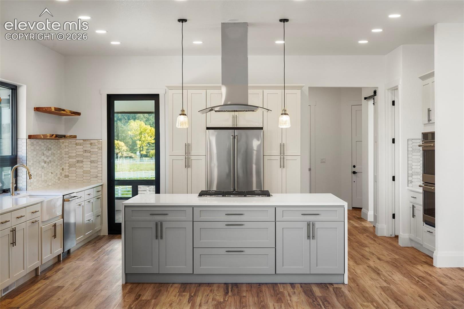 Kitchen featuring wood-finish flooring, a central island with integrated cooktop, stainless steel appliances, and shaker-style cabinetry